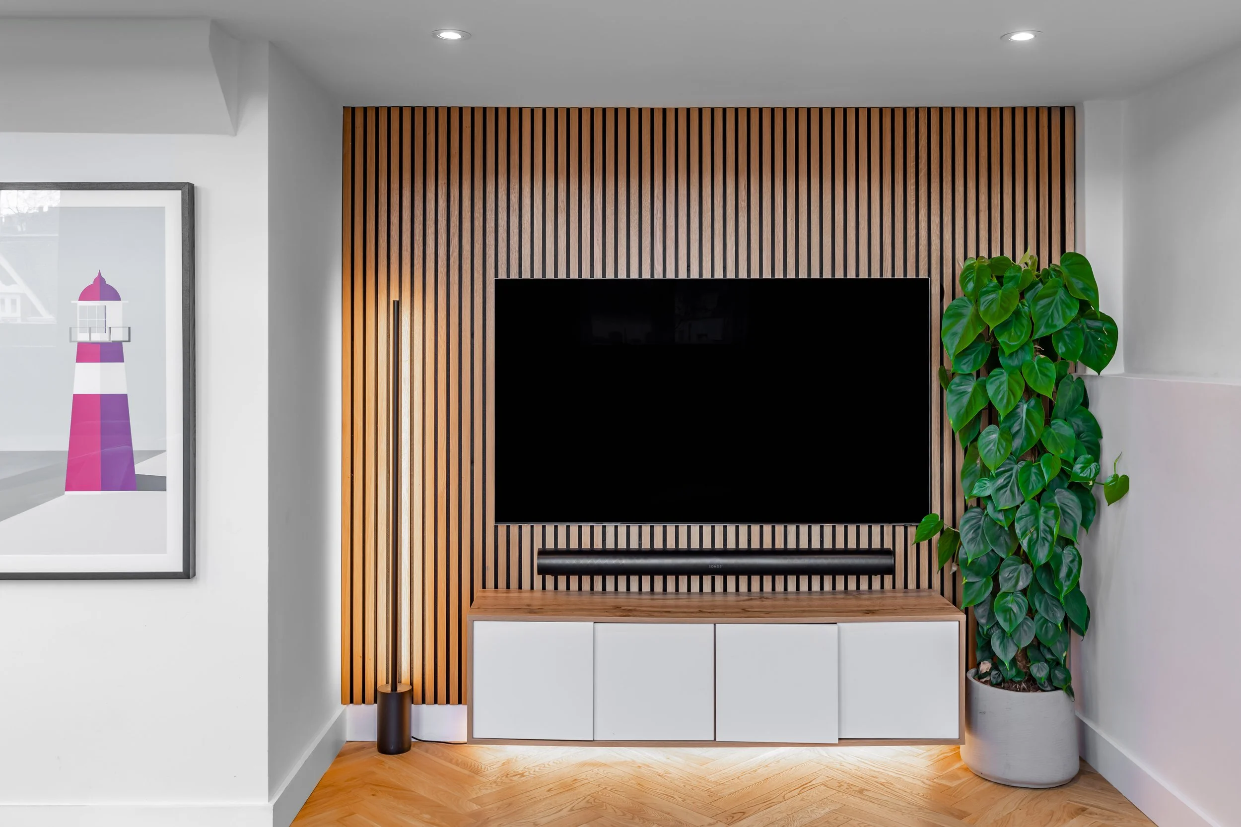 Modern living room corner with wooden slat wall, flat-screen TV, and a large potted plant.