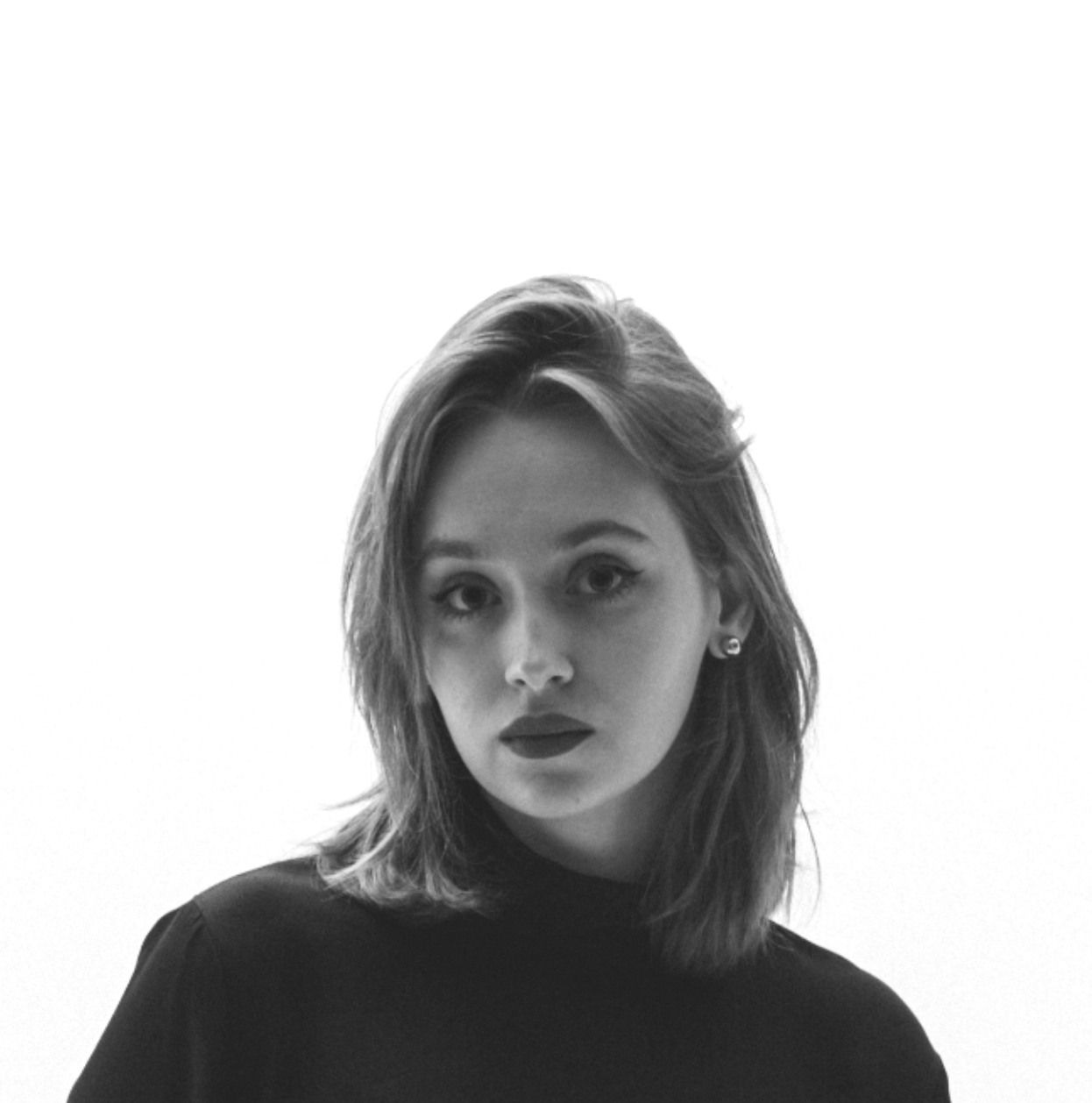 Black and white portrait of a young woman with medium-length wavy hair, dark lipstick and a black top, against a light background.