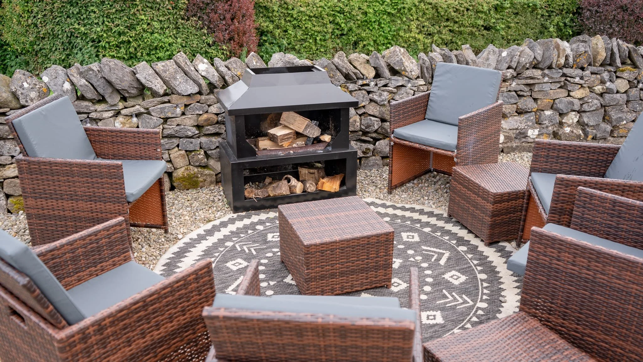 Outdoor seating area with wicker chairs and a fire pit, surrounded by a stone wall.