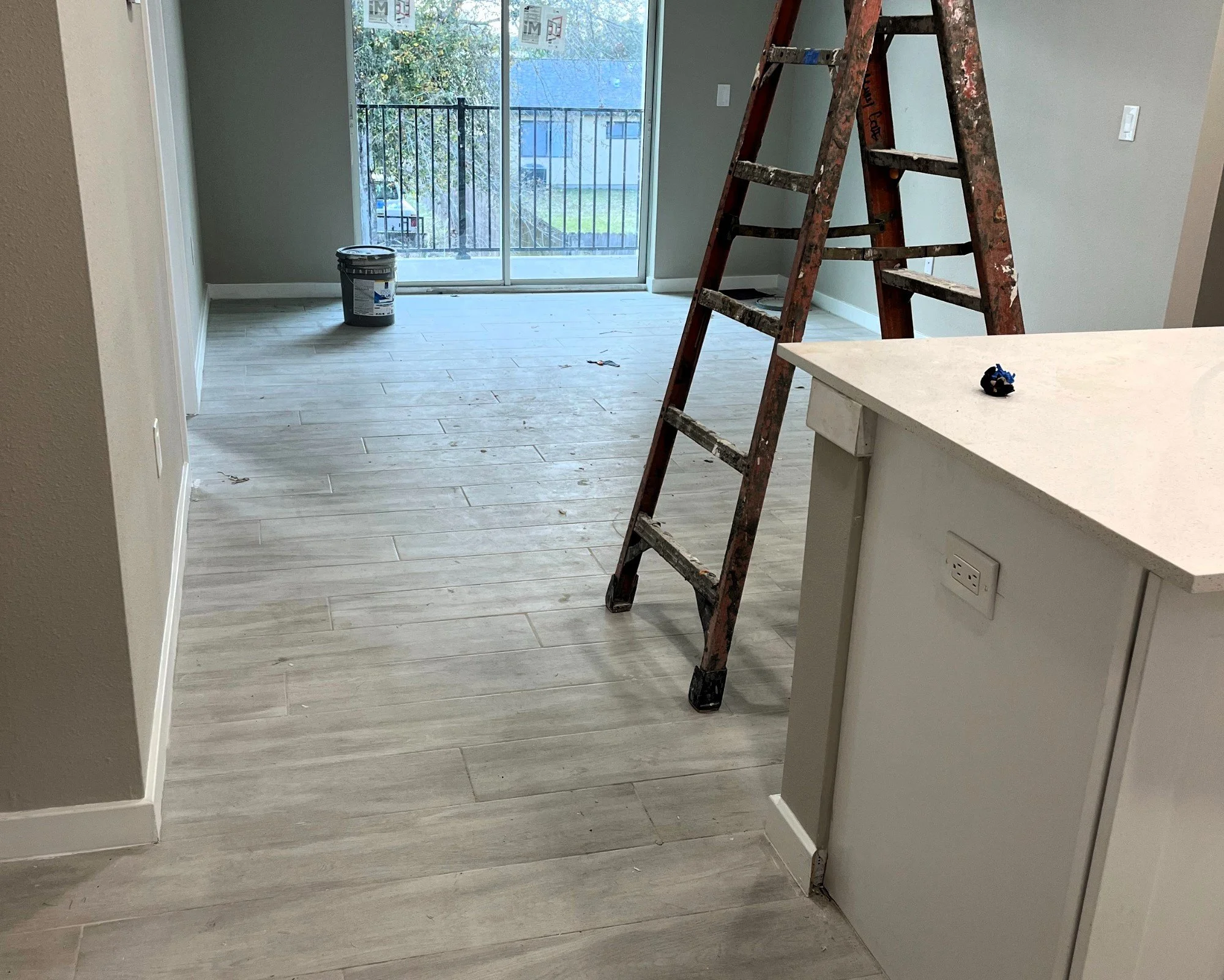 Interior of a partially renovated room with a ladder, bucket, and light-colored wood flooring.