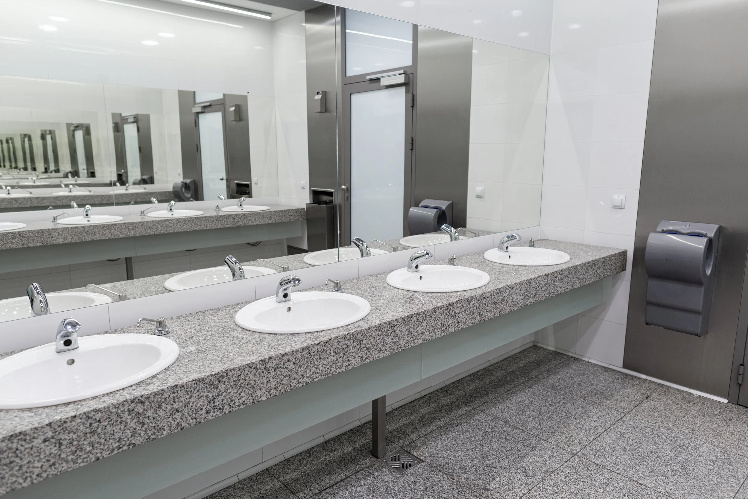 Modern public restroom with multiple sinks, mirrors, and a paper towel dispenser.