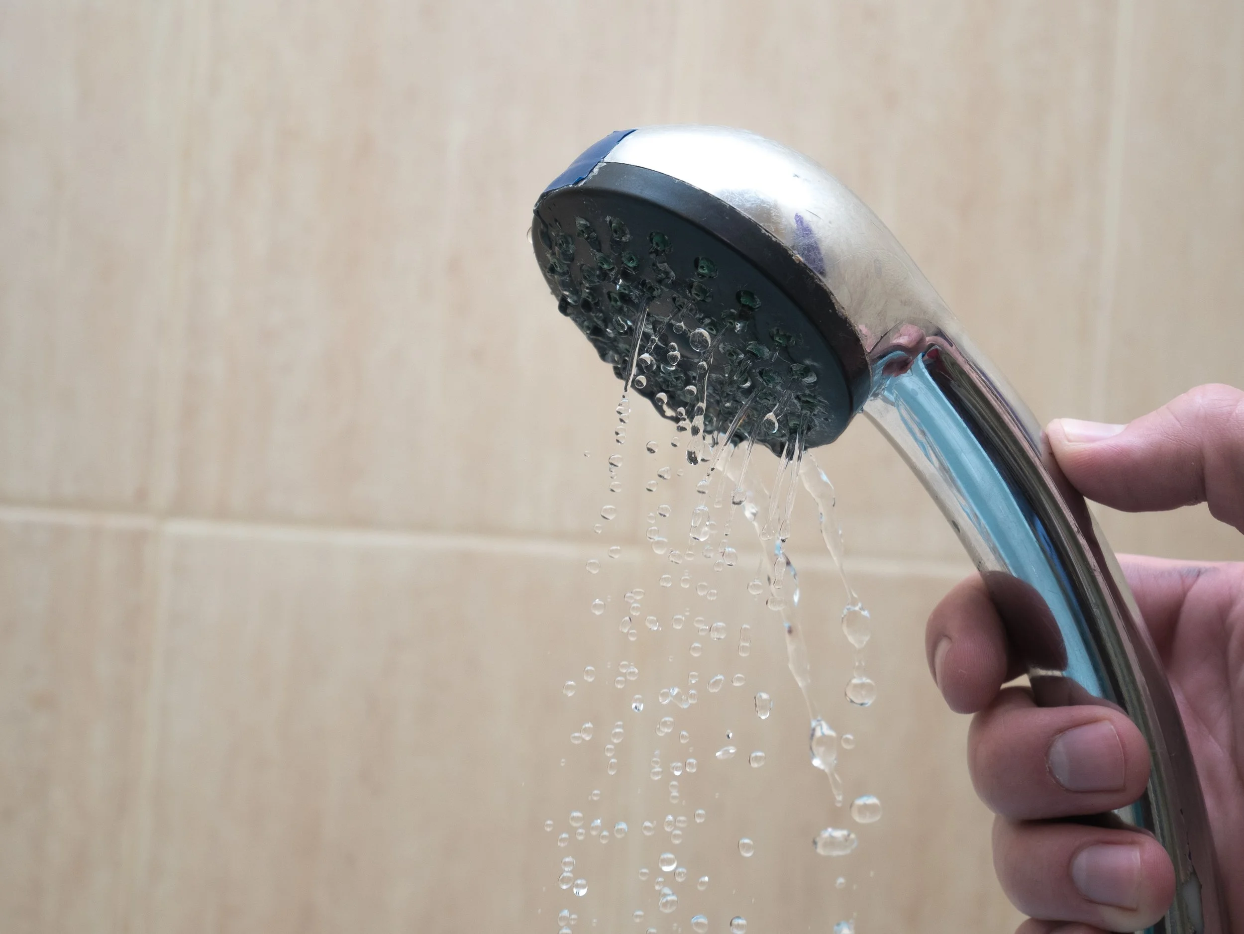 Hand holding a curved showerhead with water streaming from it.