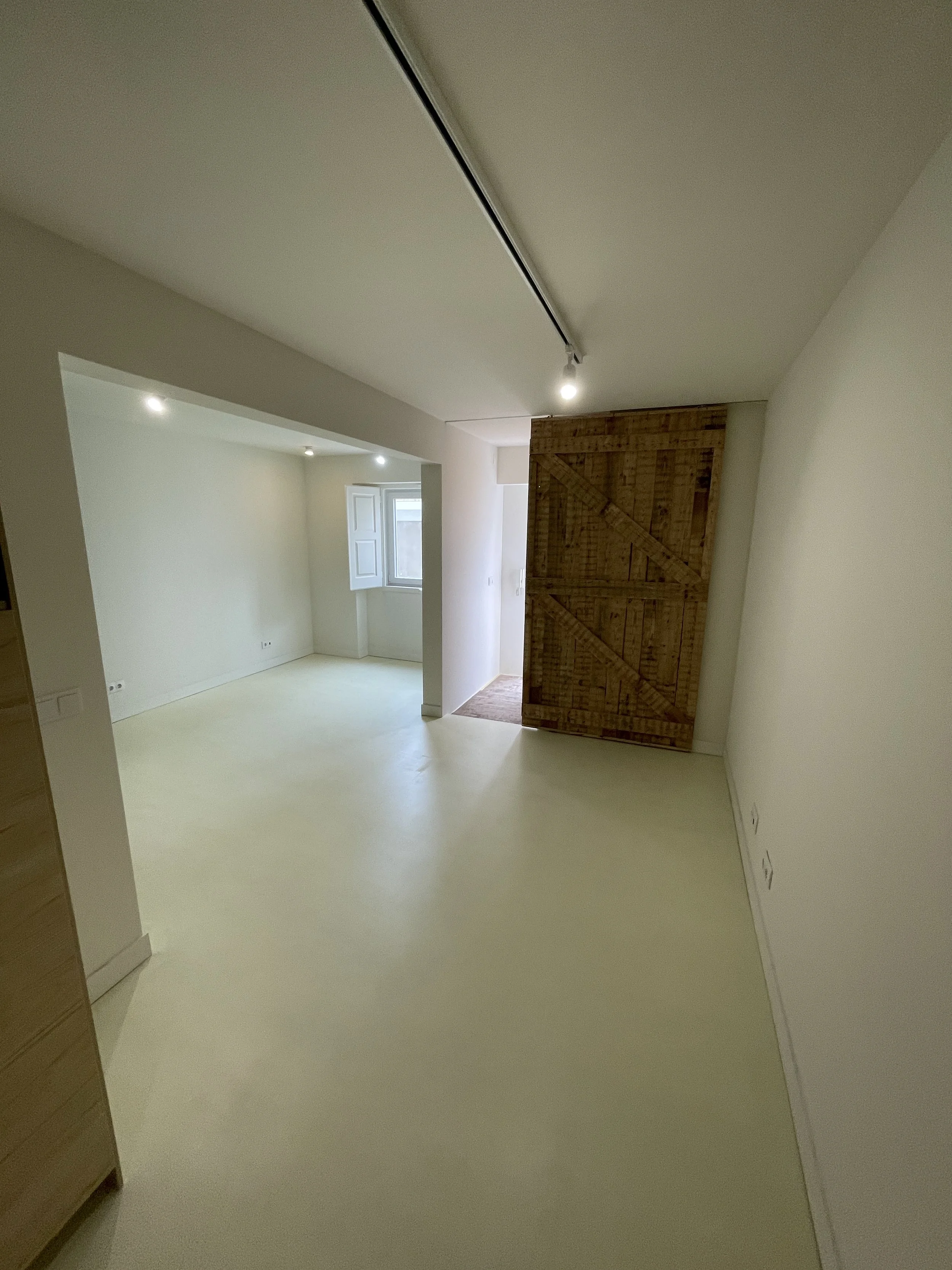 Empty room with light-colored walls and flooring, a small window, and a sliding wooden barn door.