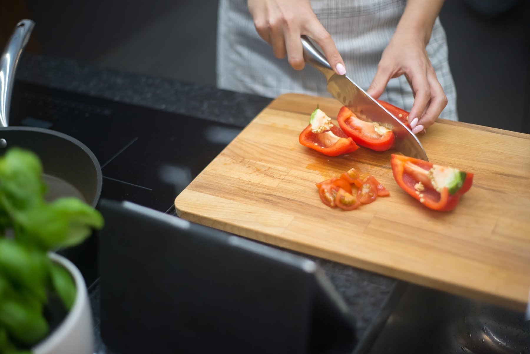 Hands slicing a red pepper on a wooden cutting board in a home kitchen