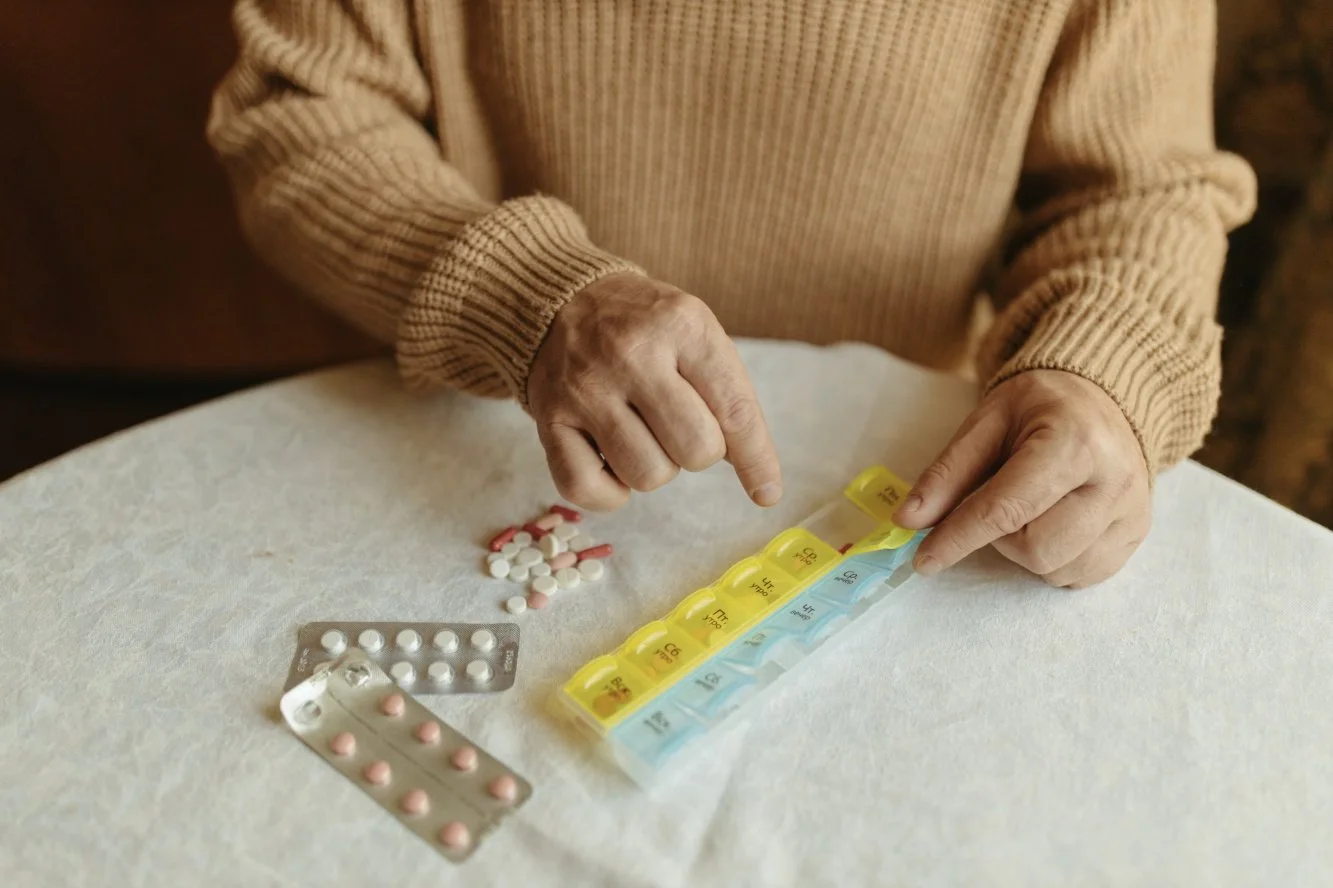 Hands organizing a weekly pill case with prescription pills laid out on a table