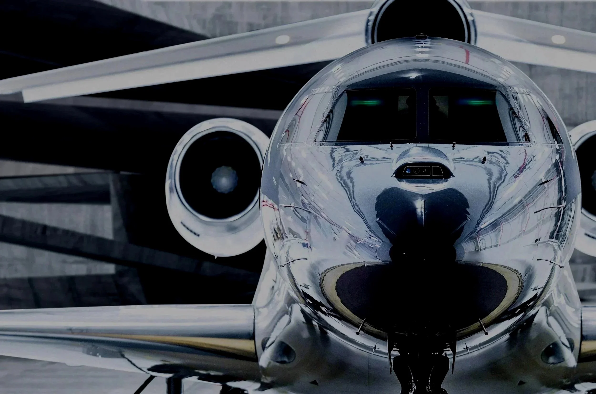 Close-up front view of a sleek, silver private jet parked on the tarmac, with a reflective surface and two engines visible on the sides.