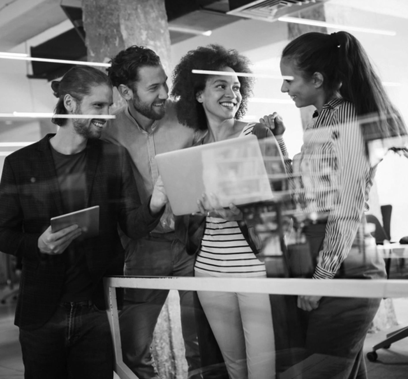 A diverse group of five coworkers gathered around a table, smiling and engaging in conversation in an office setting.