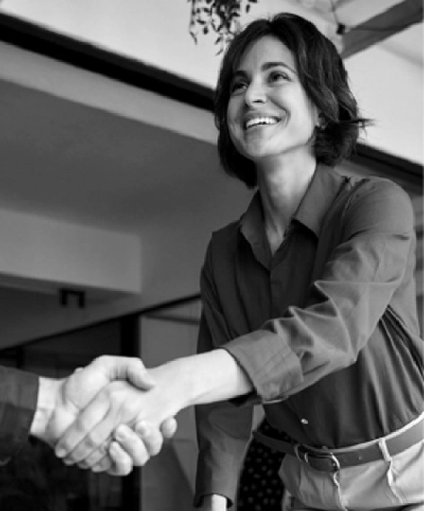 A woman with short dark hair smiling and shaking hands with someone in a professional setting.
