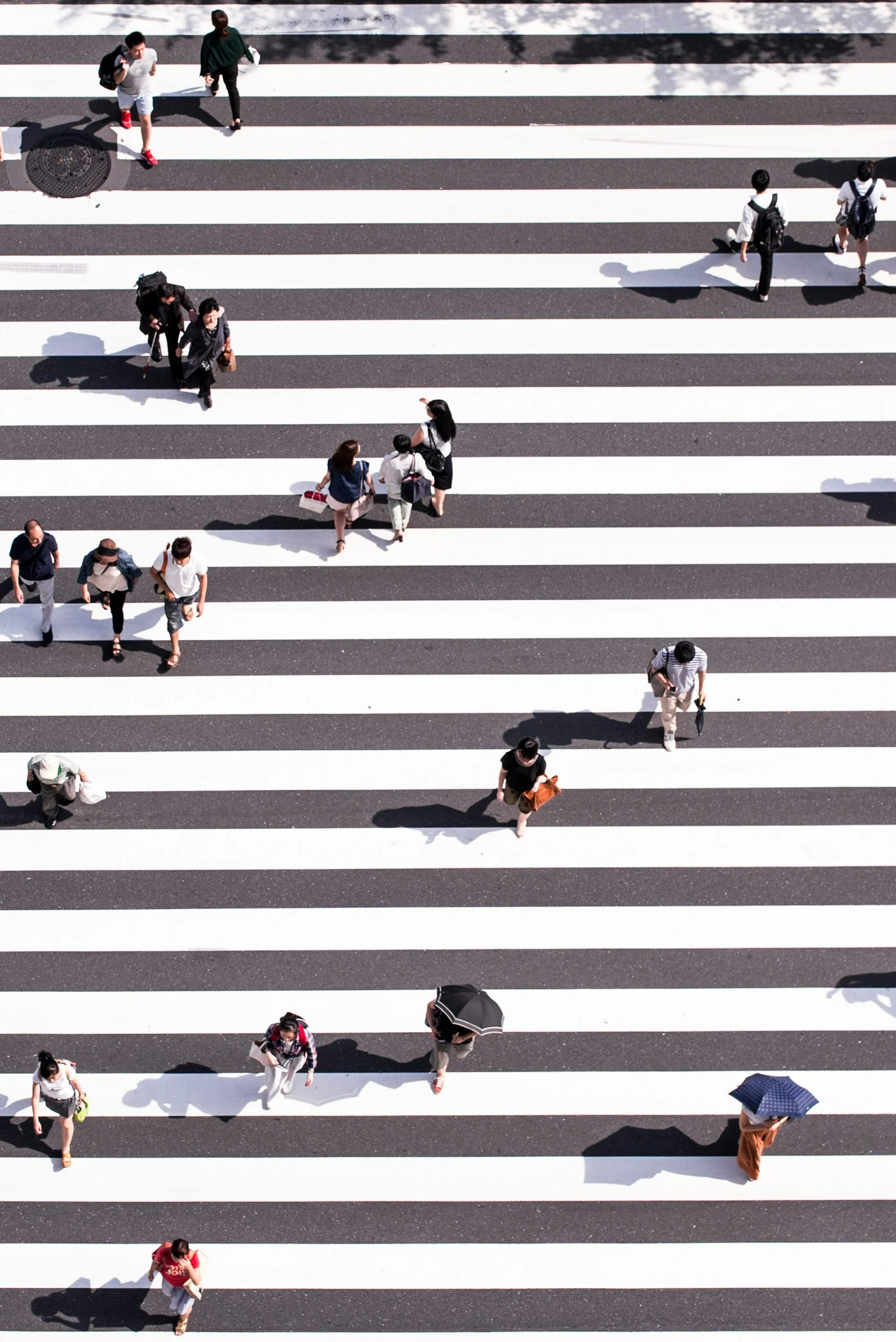 People crossing a street at a zebra crosswalk on a sunny day, seen from above.
