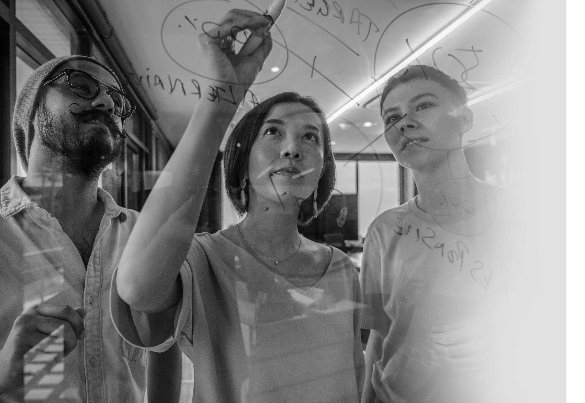 Three people writing on a transparent glass board with marker, discussing ideas in an office.