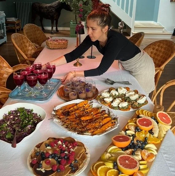 la cheffe privé entrain de déposer un brunch avec divers plats colorés et végétaux disposés sur une table de salle à manger