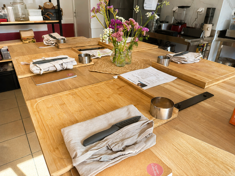 ilôt central bois dans un laboratoire de cuisine avec atelier en préparation planche à découper bois, tablier lin, fleurs en centre de table