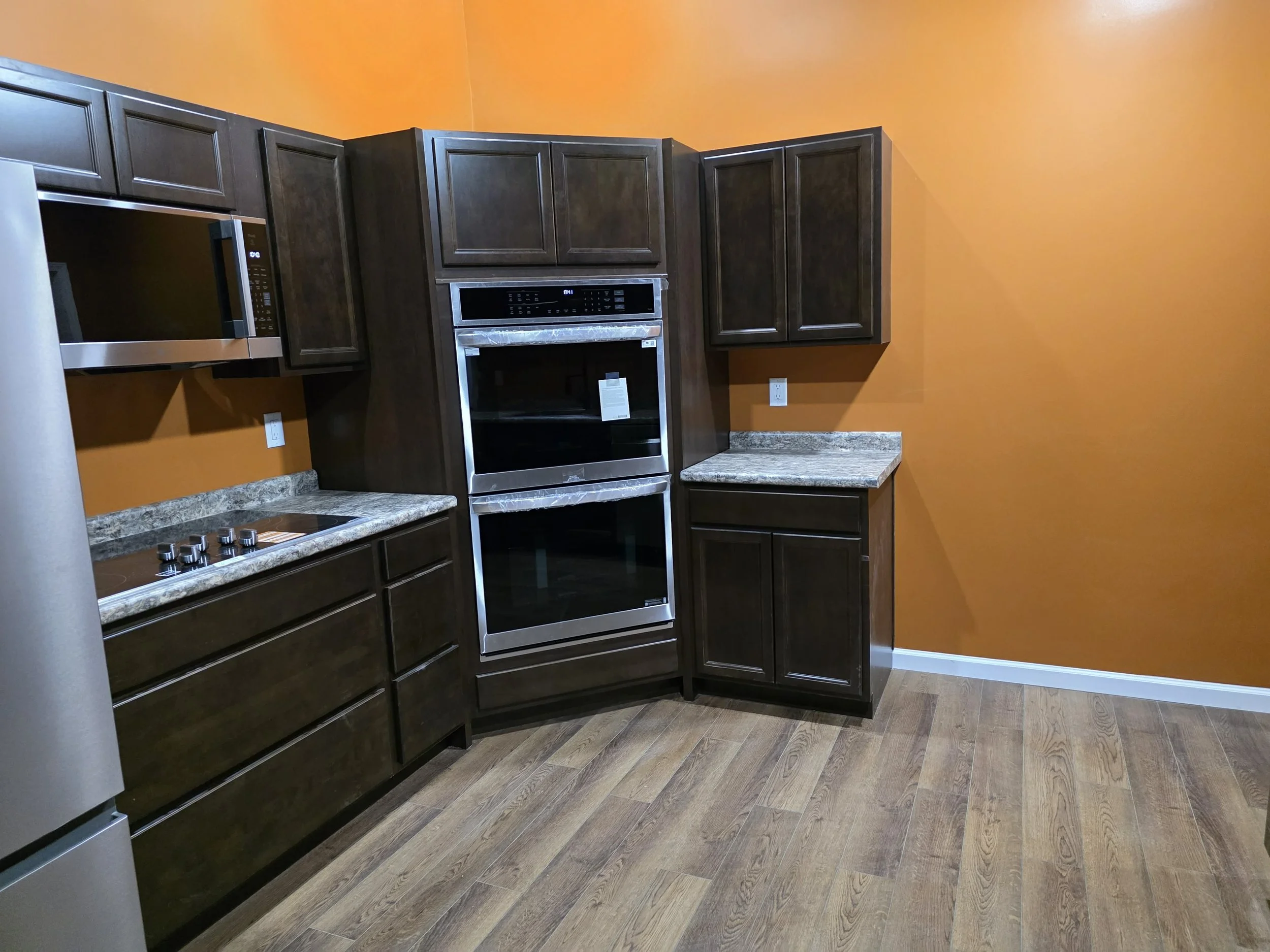 Kitchen with dark cabinets, orange walls, granite countertops, and built-in microwave and oven.