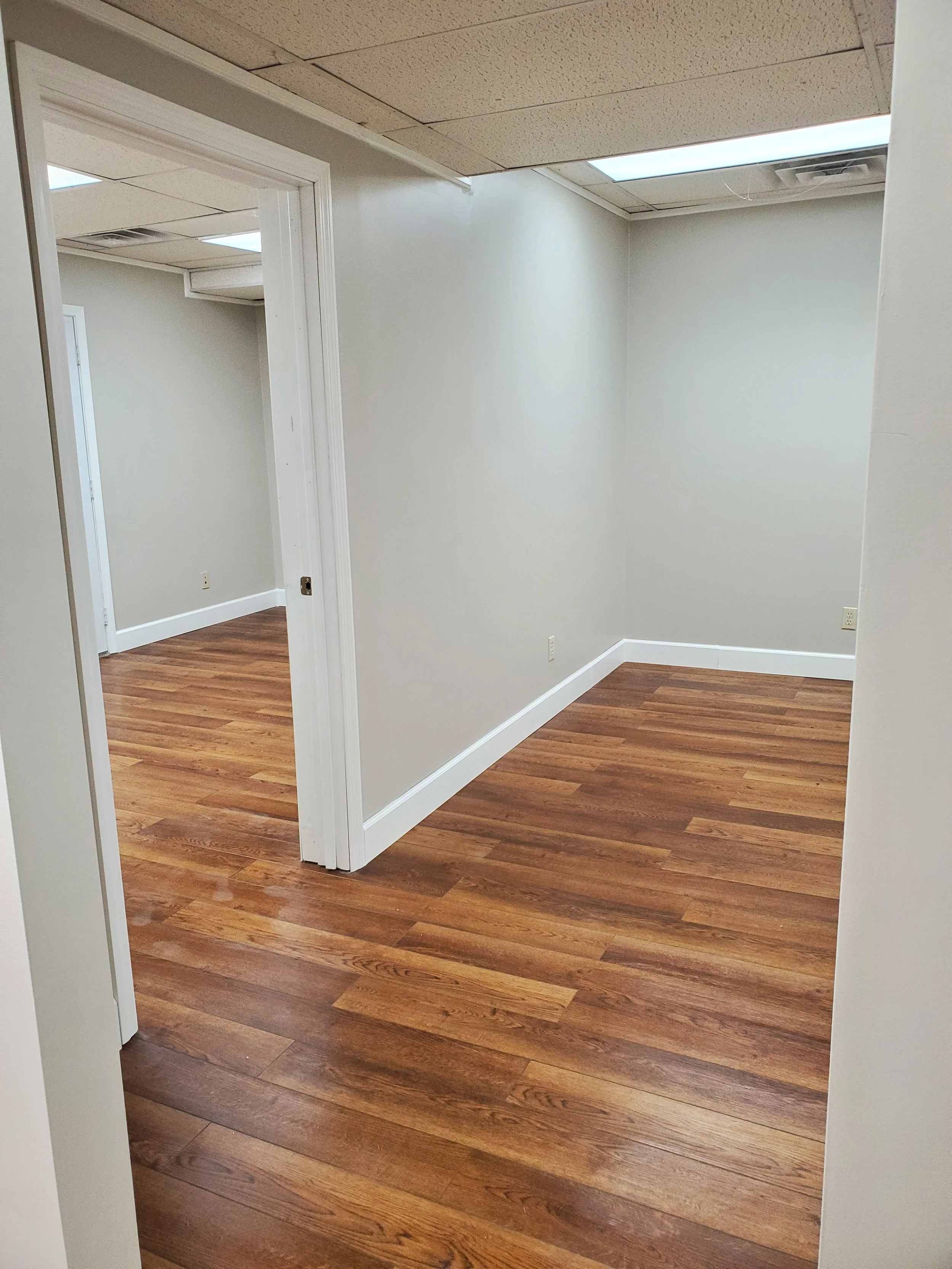 Empty room with light gray walls, white trim, and dark brown wooden floors.