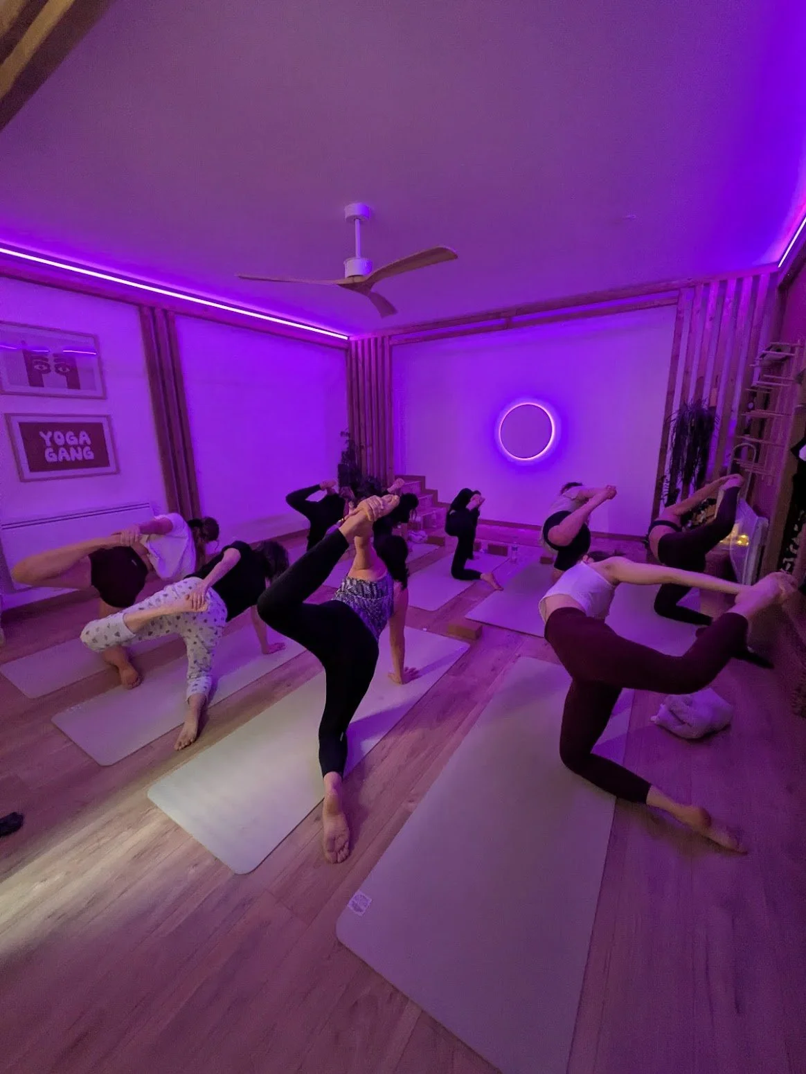 Groupe de personnes pratiquant le yoga vinyasa à Lyon dans une salle avec éclairage violet, certains en équilibre sur un pied avec la jambe levée à Lyon Croix-Rousse.