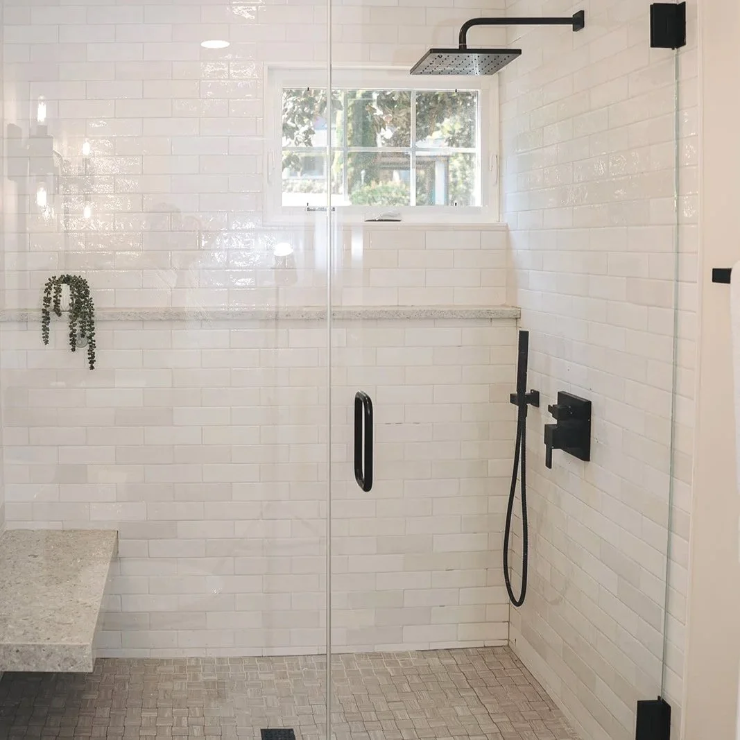 Modern walk-in shower with black fixtures, a rainfall showerhead, and a small window, with white subway tiles on the wall and a granite bench.
