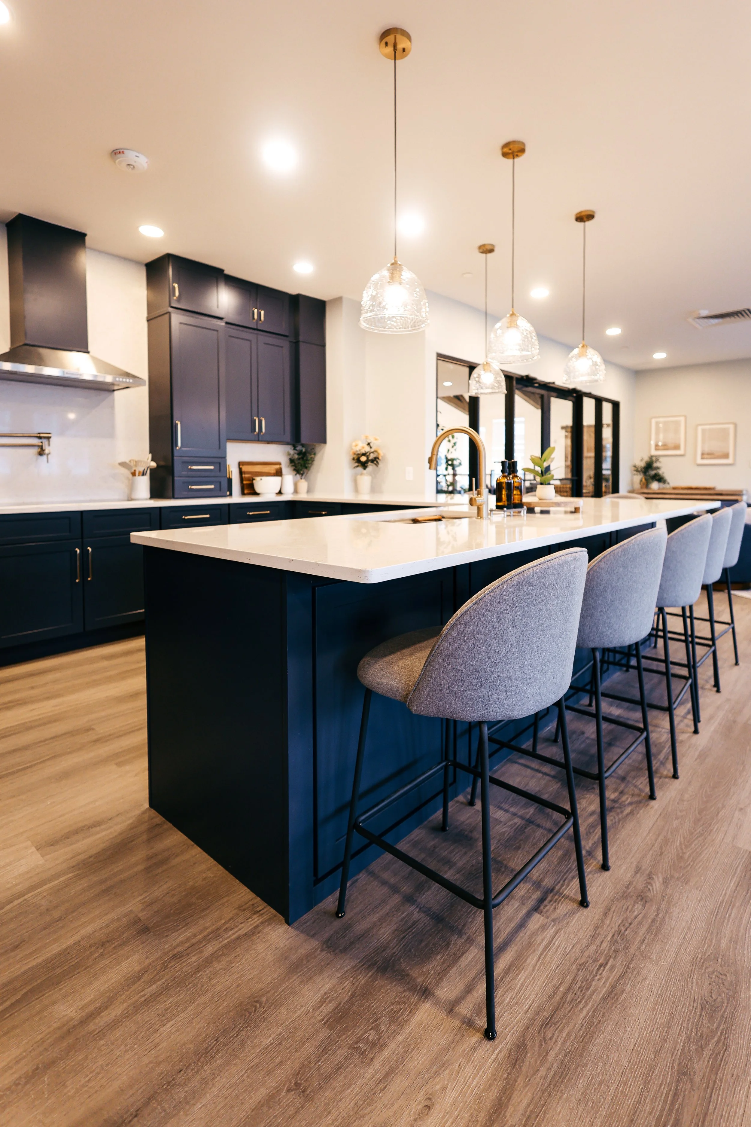 Modern kitchen with navy blue cabinets and a white island counter with bar stools, pendant lighting, and light wood flooring.
