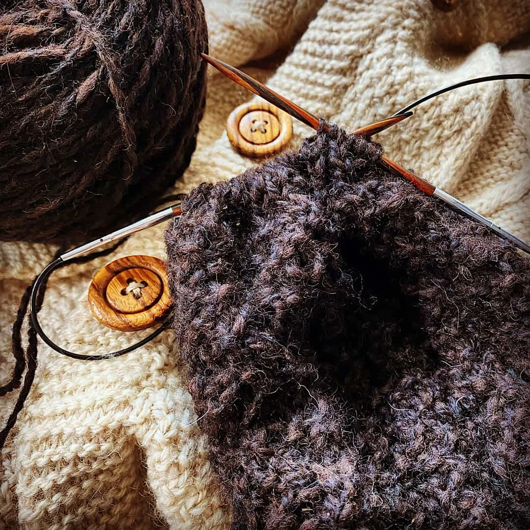 Stricknadel, Wollknäuel, gestricktes Stück, große Holzdurchmesserknöpfe, Wolldecke, Kleidung in warmen Farben.