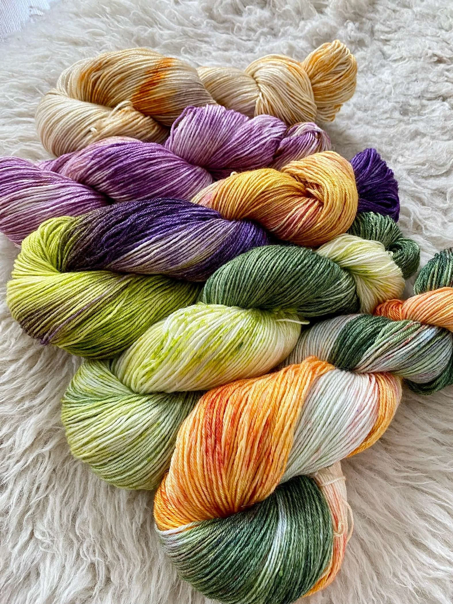 Mehrfarbige handgefärbte Strickwolle in verschiedenen Farben, die auf einer weißen, geflammten Oberfläche liegen.