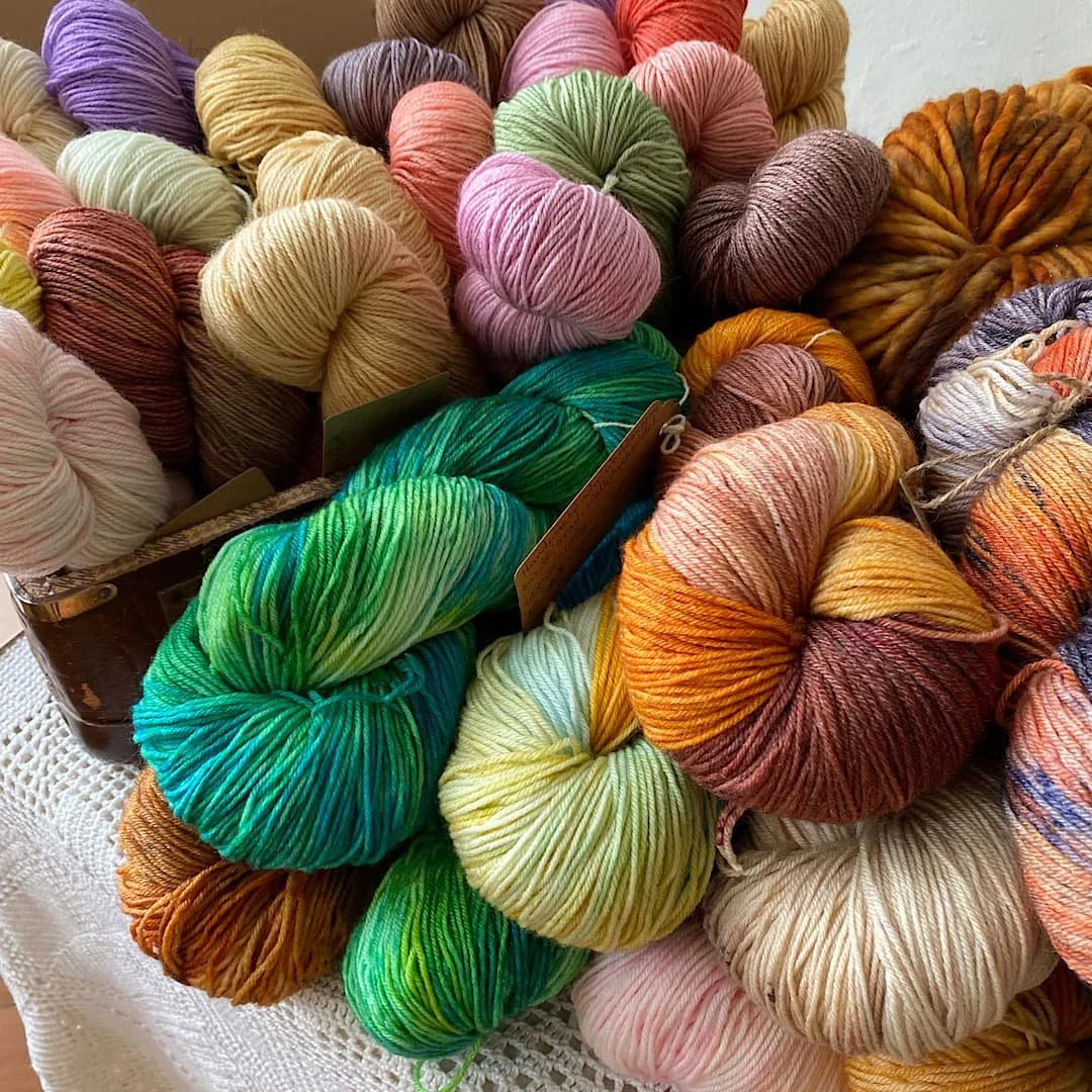 Bunte Wollknäuel in mehreren Farben, darunter Grün, Pink, Orange, Braun und Creme, auf einer Tischdecke