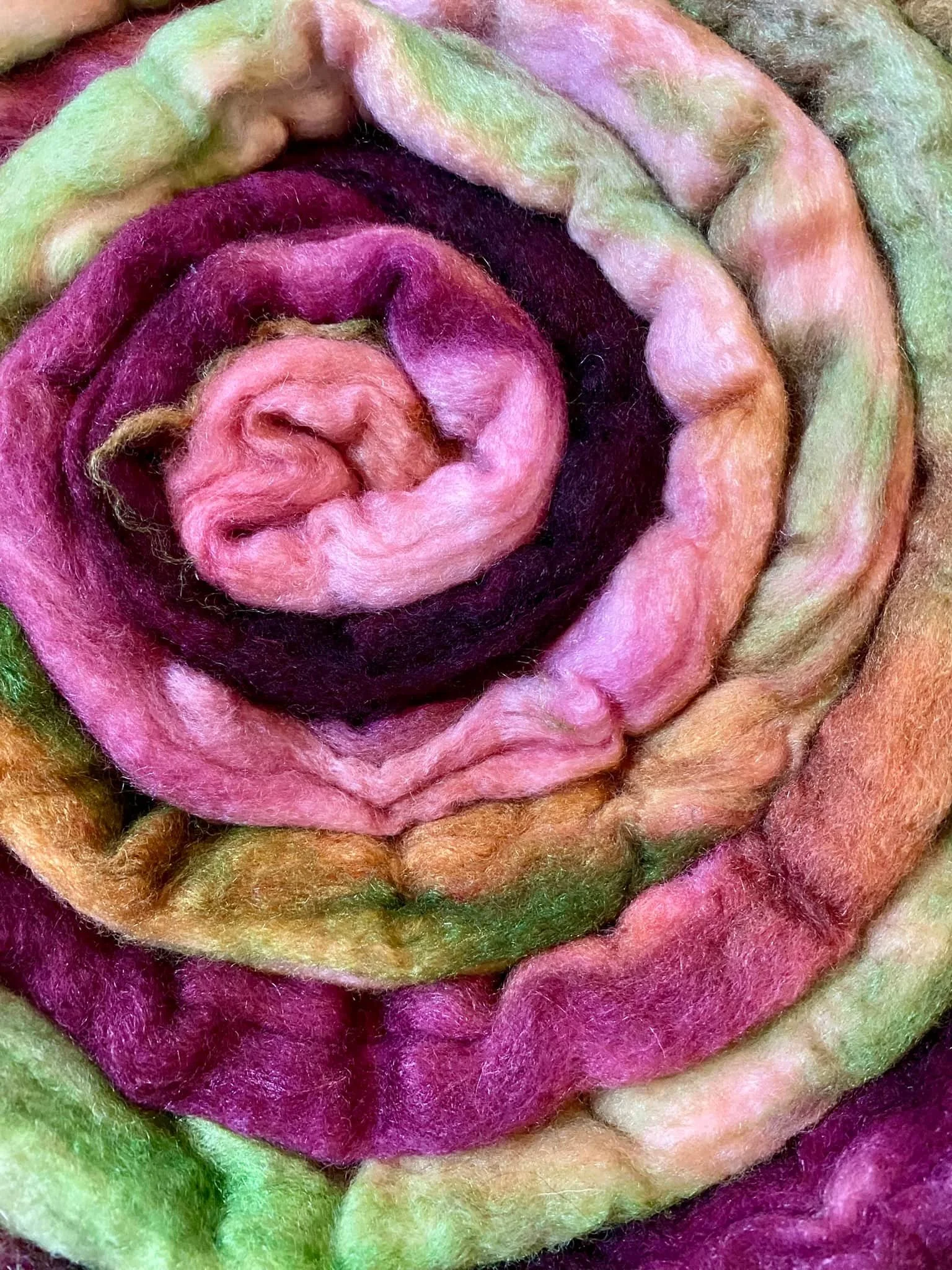 Bündel bunter Filzfasern in Rosa-, Lila-, Grün- und Orange-Tönen, kunstvoll spiralförmig angeordnet.