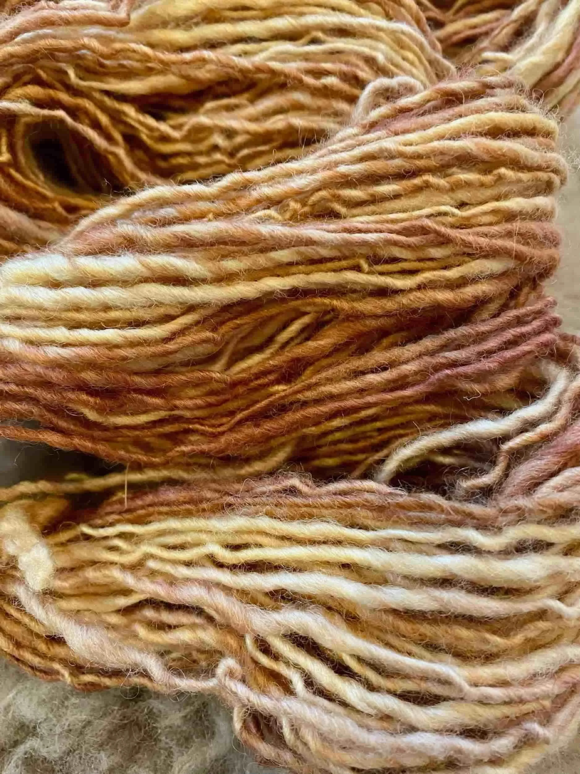 Nahaufnahme von mehreren Strängen Wolle in warmen Farbtönen wie Beige, Orange und Braun.