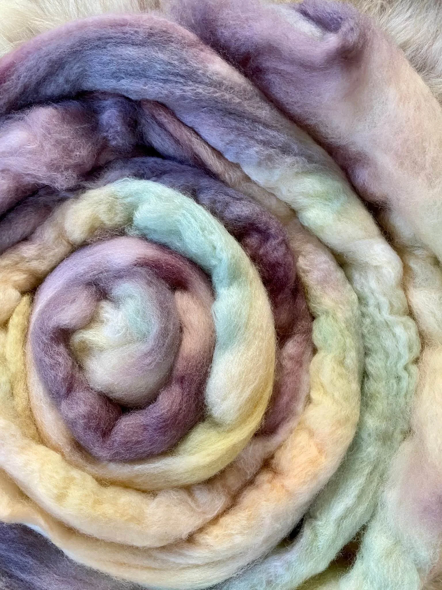Bündel aus buntem, weichem Filz- oder Wollefasermaterial, spiralförmig aufgerollt, in Pastellfarben wie Gelb, Lilau, Grün und Creme.