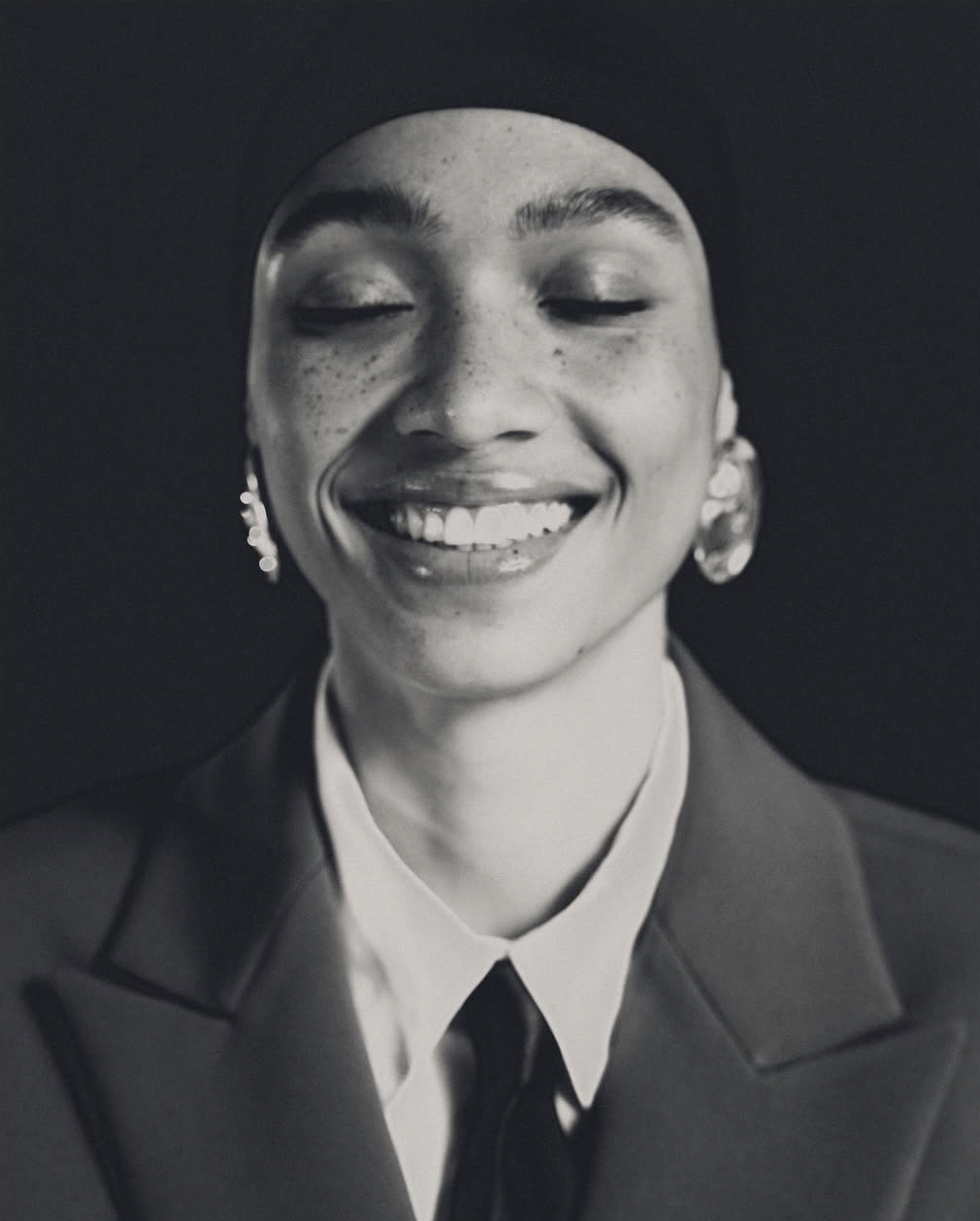 Portrait en noir et blanc d'une femme souriant avec des boucles d'oreilles et portant un uniforme ou une veste.