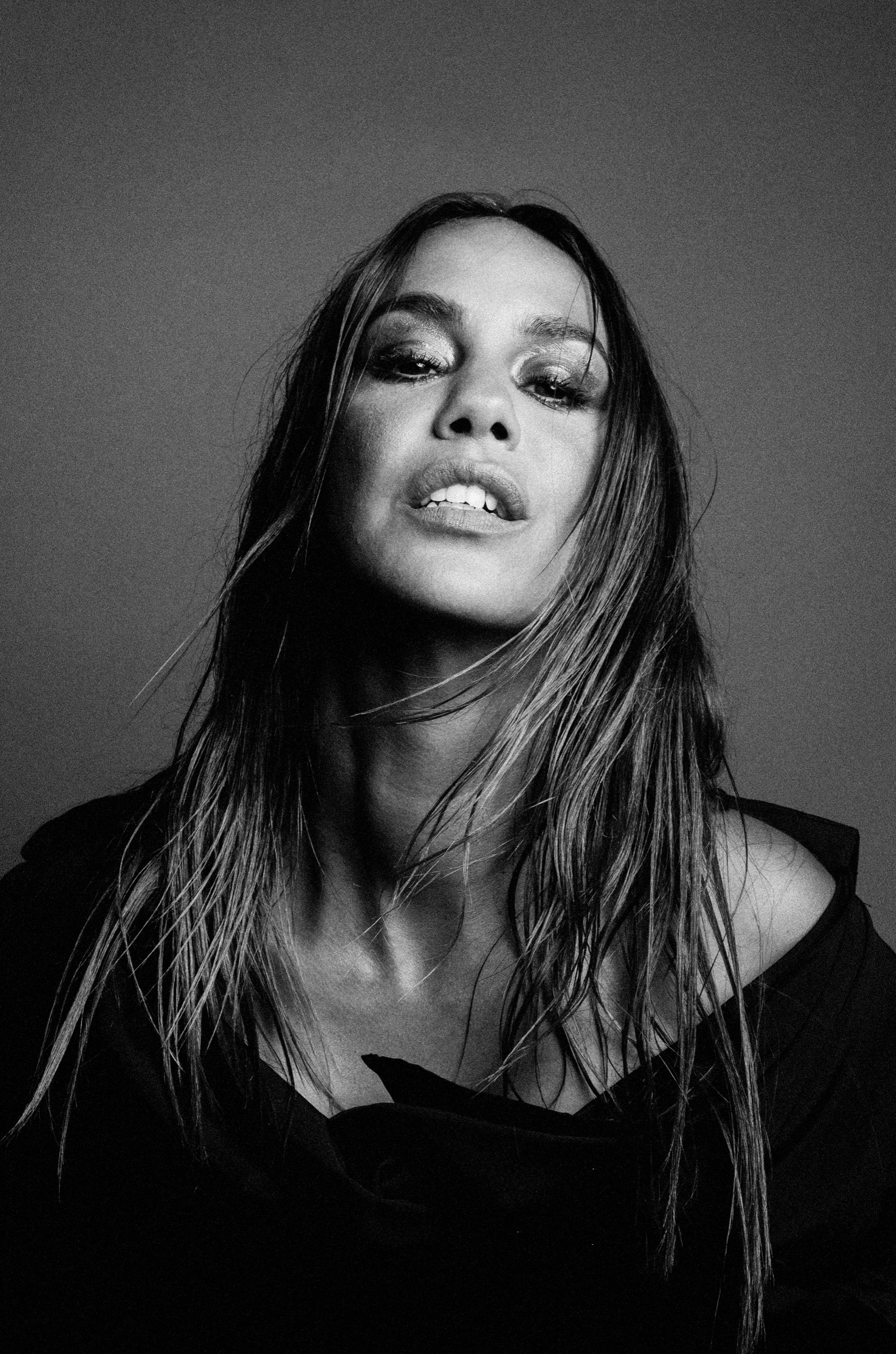 Portrait en noir et blanc d'une femme avec des cheveux mouillés, portant un vêtement sombre, regardant vers le haut avec une expression confiante. Alice Belaïdi