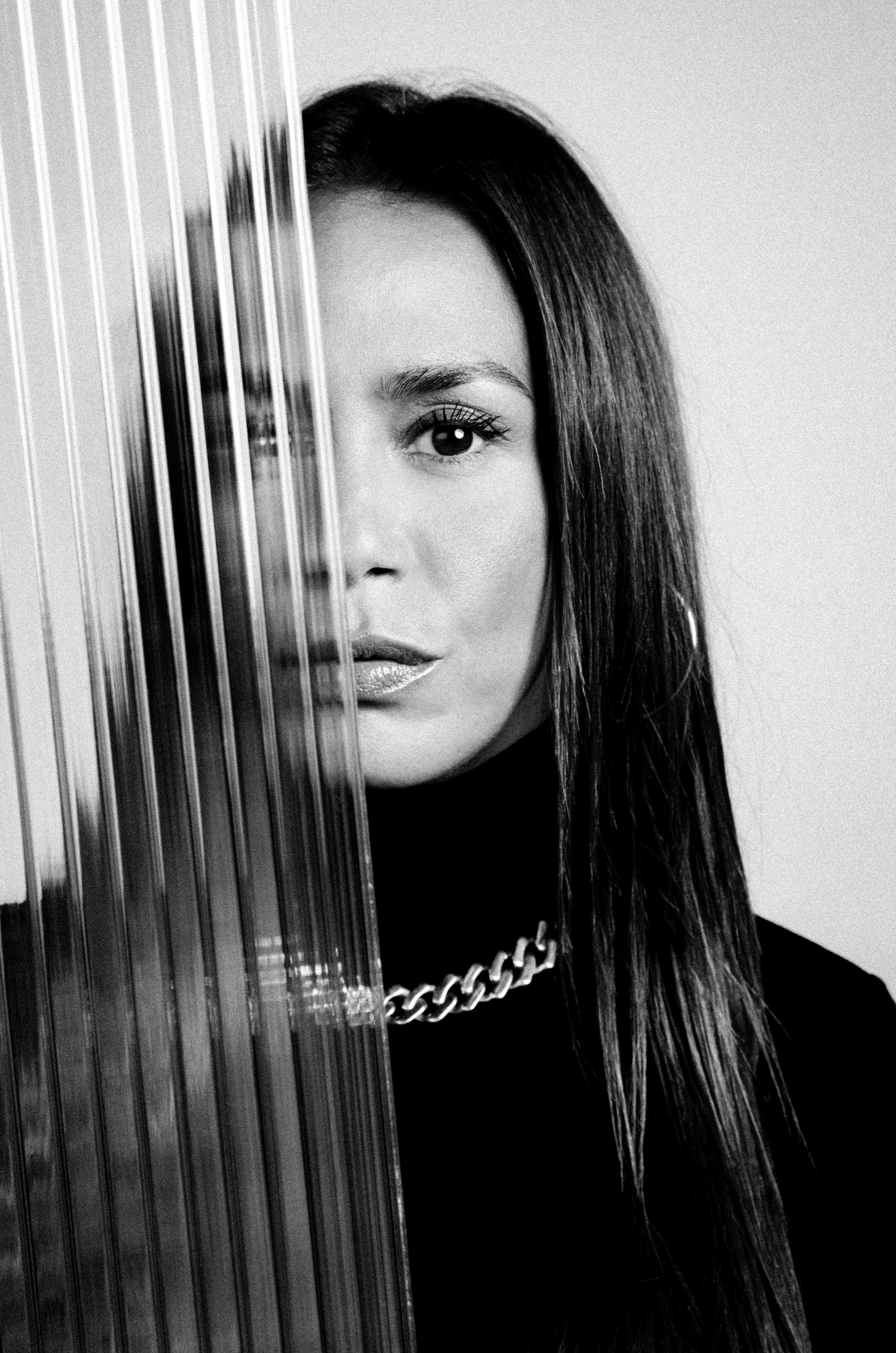 Portrait d'une femme avec la moitié de son visage derrière un panneau transparent avec des rayures verticales. En noir et blanc.