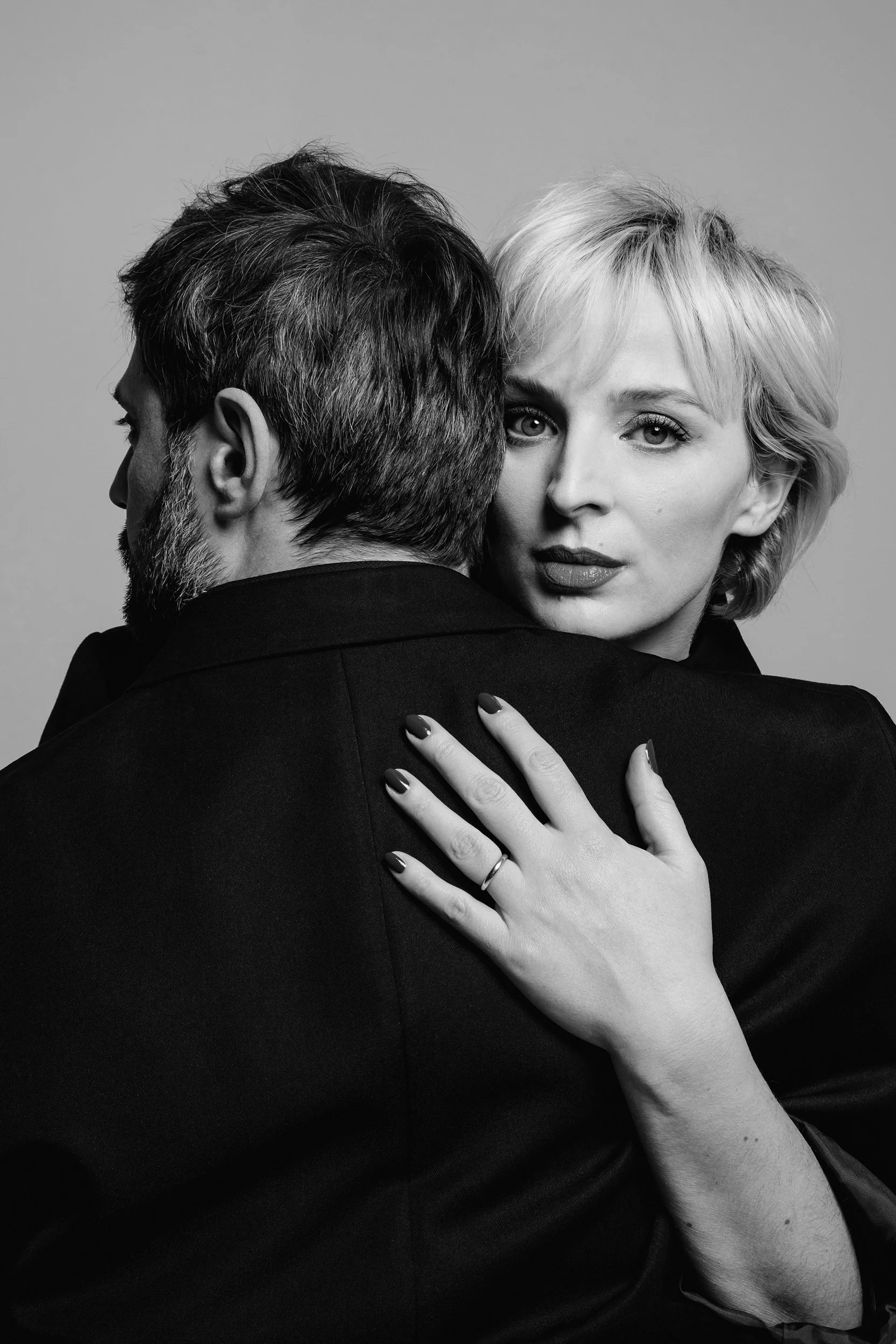 Madame, Monsieur. Portrait en noir et blanc d'une femme avec cheveux blonds courts, regardant vers l'appareil, embrassant ou tenant un homme dont le visage est de profil, avec une barbe grise, la main de la femme posée sur le dos de l'homme.