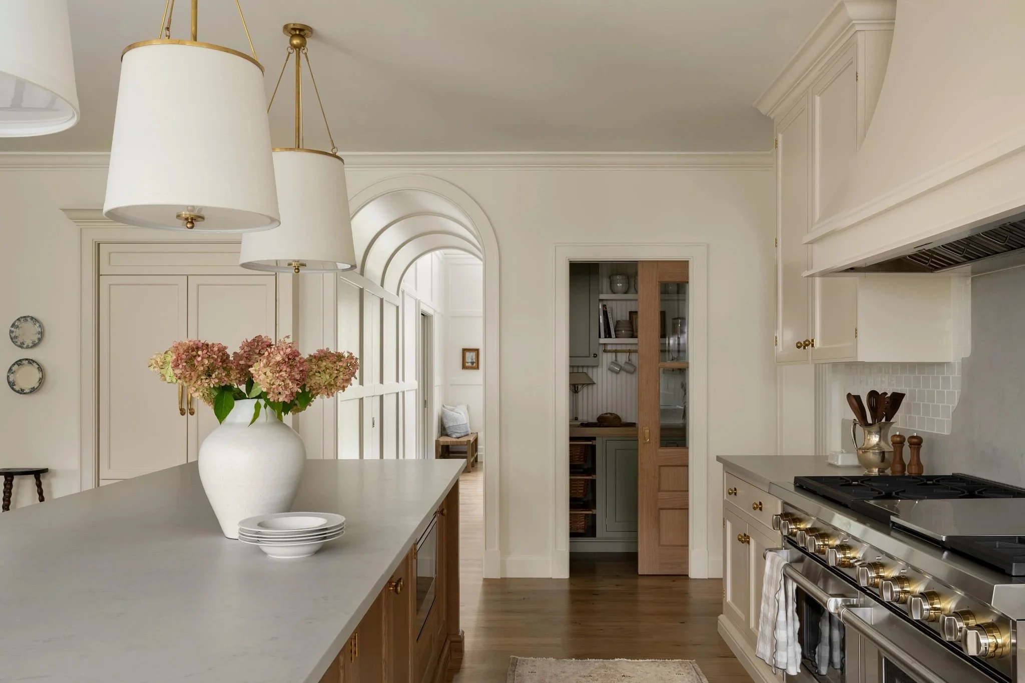 A spacious, bright kitchen with white cabinets, a large kitchen island with a vase of pink flowers, a stainless steel stove, and pendant lights hanging from the ceiling.
