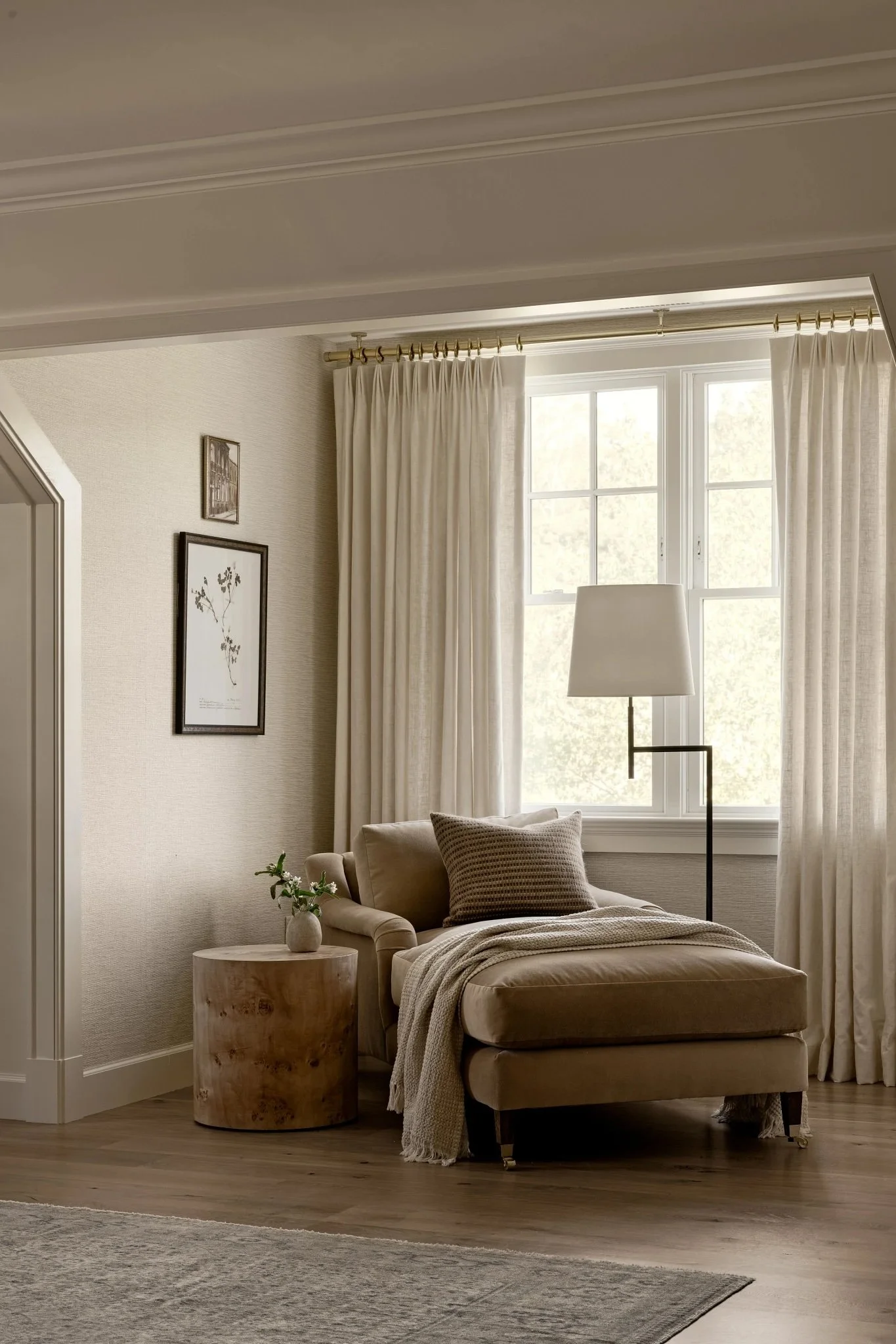 Cozy beige living room corner with armchair, side table with plant, window with cream curtains, and floor lamp.