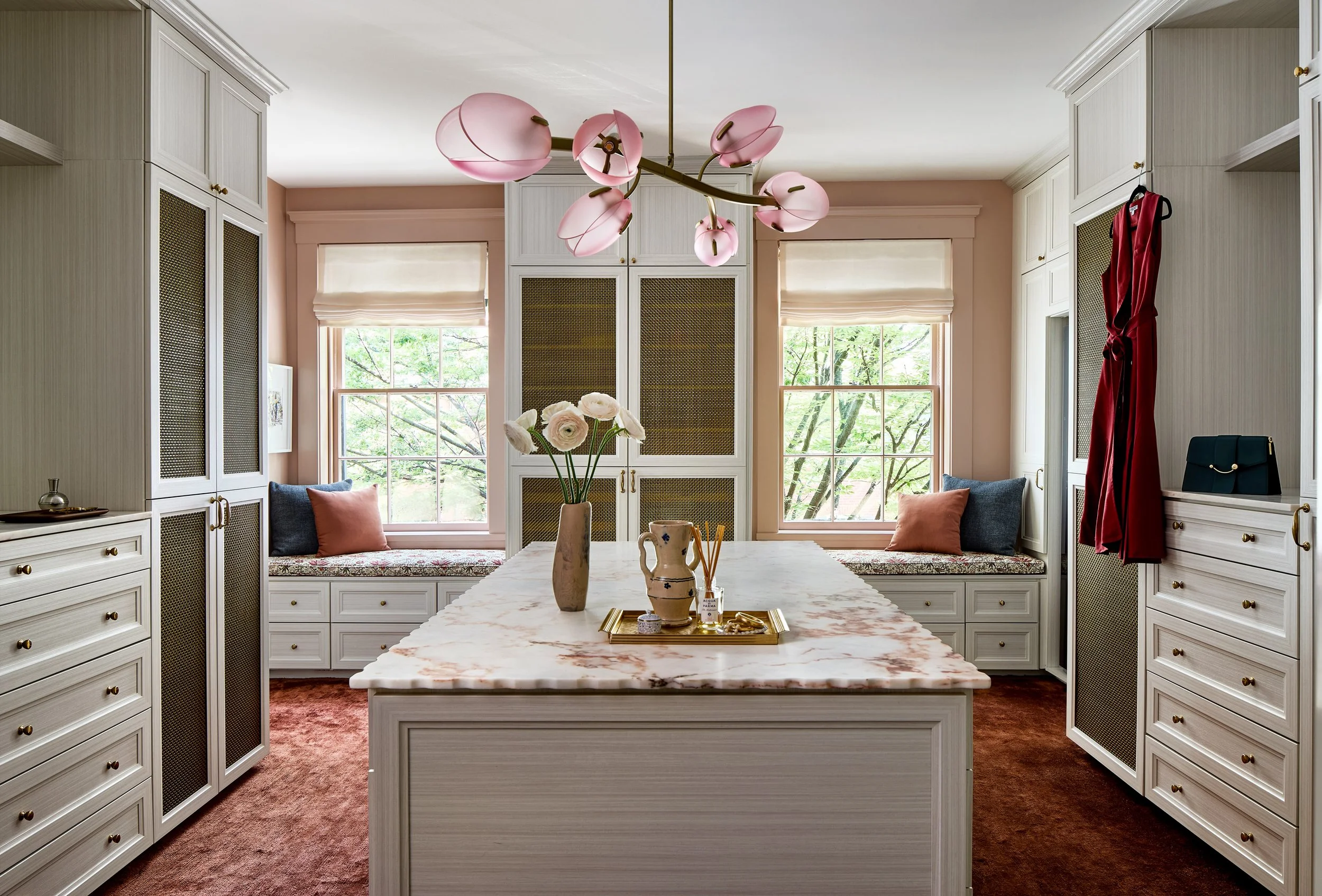 Kitchen with built-in cabinetry, a marble island, pink chandelier, flowers, and windows with window seats.