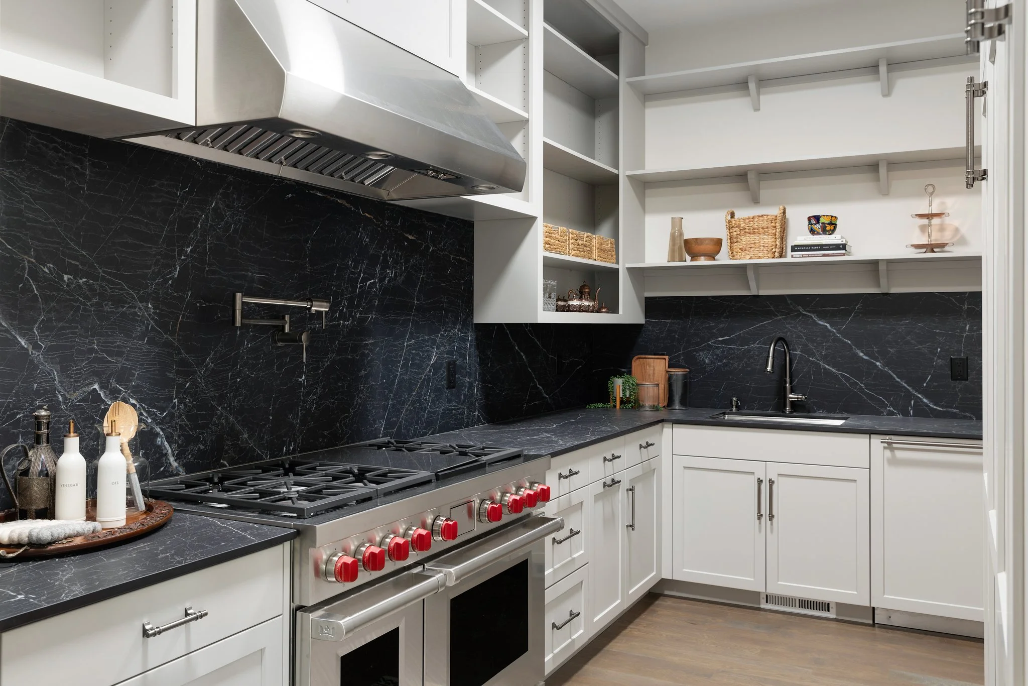 Modern kitchen with black marble backsplash, white cabinets, stainless steel appliances, and open shelving with decorative items.