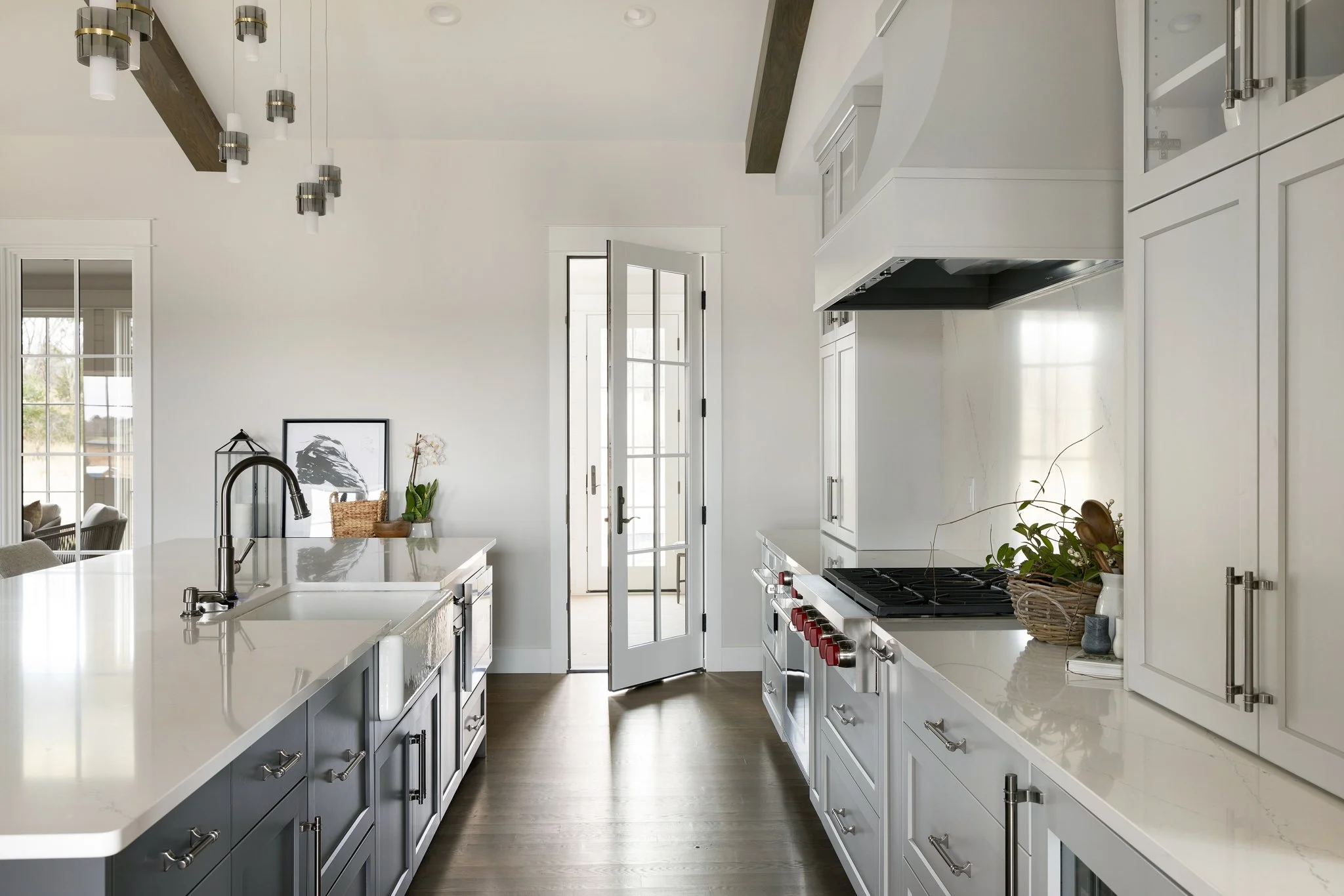 Modern white kitchen with a central island, stainless steel appliances, and large windows letting in natural light.