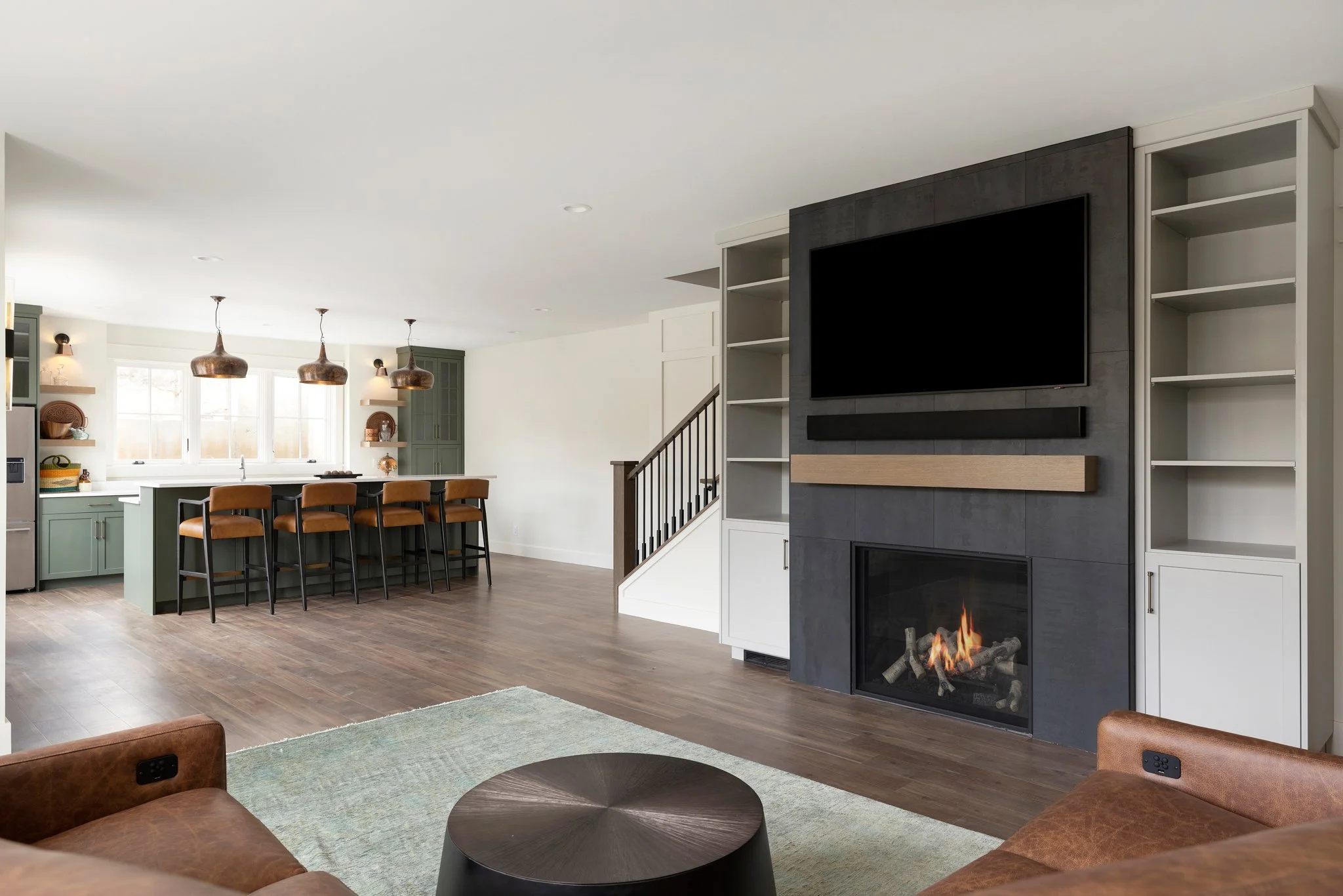 Modern open-concept living room and kitchen with a fireplace, large TV, bookshelves, and a kitchen island with barstools.