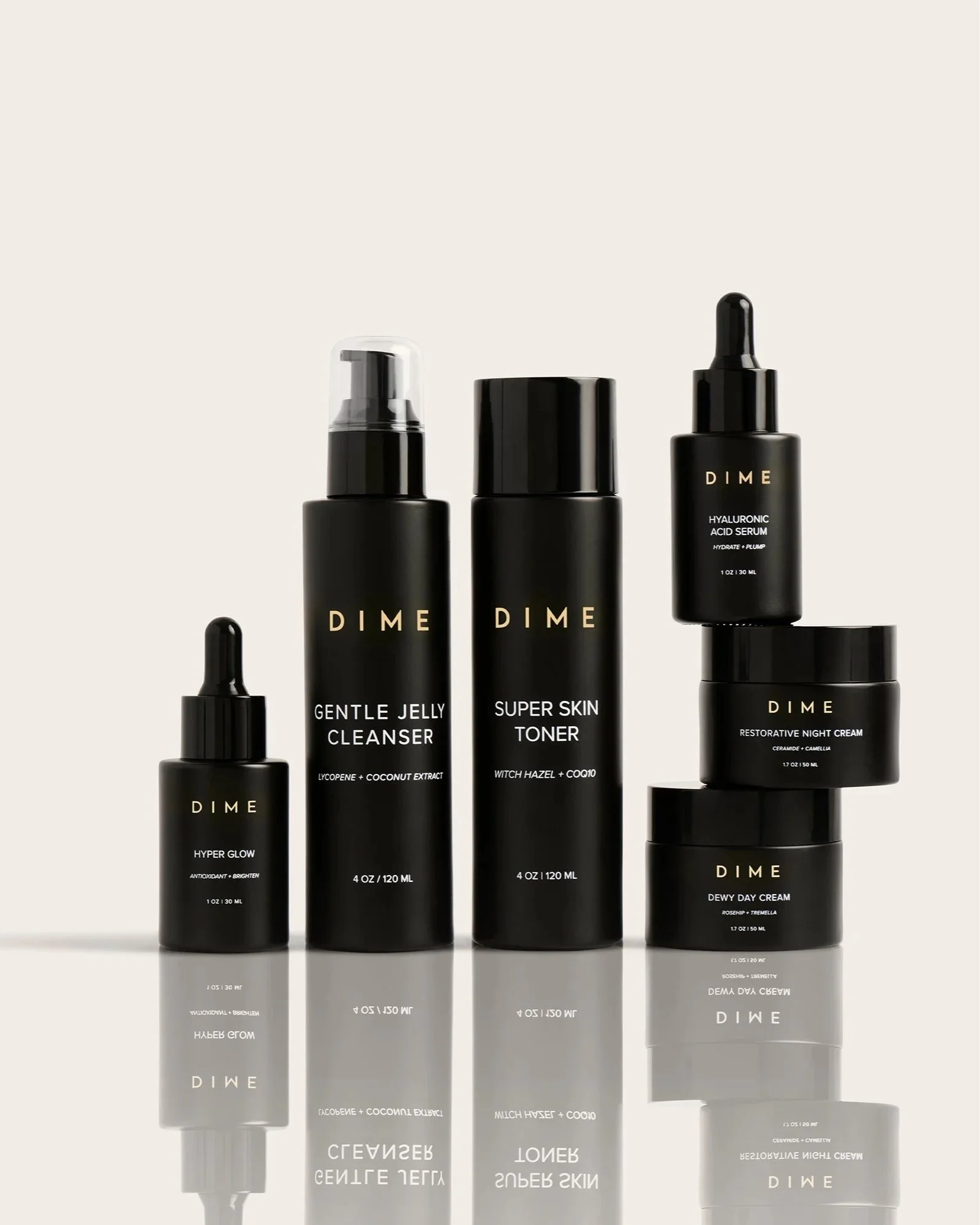 A collection of black skincare bottles with gold text, including a gentle jelly cleanser, super skin toner, hyaluronic acid serum, restorative night cream, hyper glow, dewy day cream, and others, arranged on a reflective surface with a plain light background.