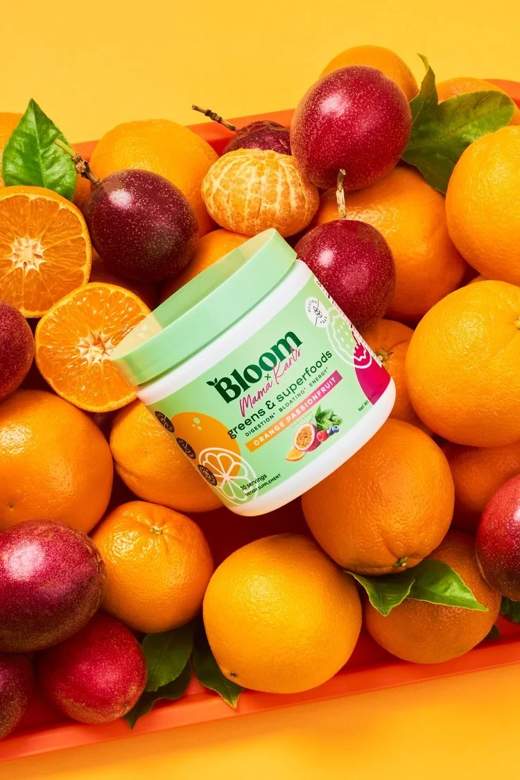 A bottle of Bloom Mama Lar Greens & Superfoods with orange flavor on a bed of oranges, blood oranges, and leaves.