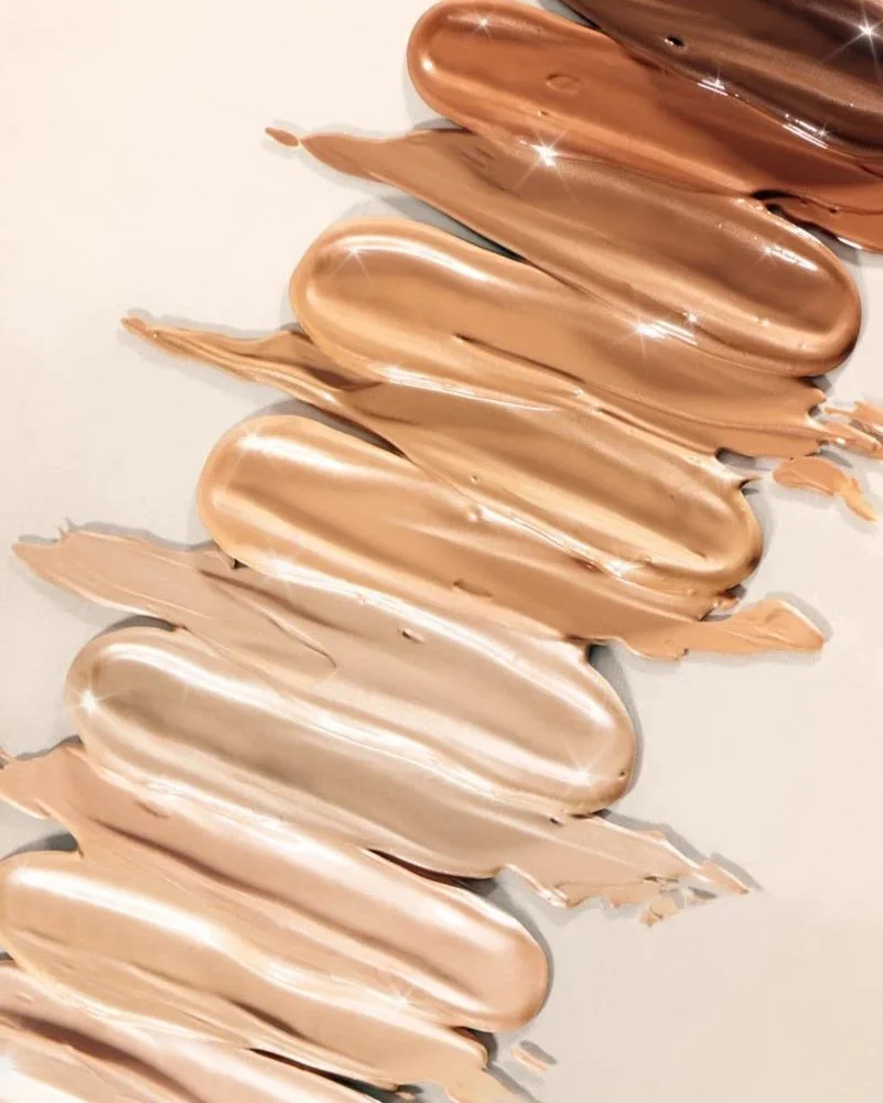 Multiple swatches of light and dark beige makeup foundation spread on a white surface.