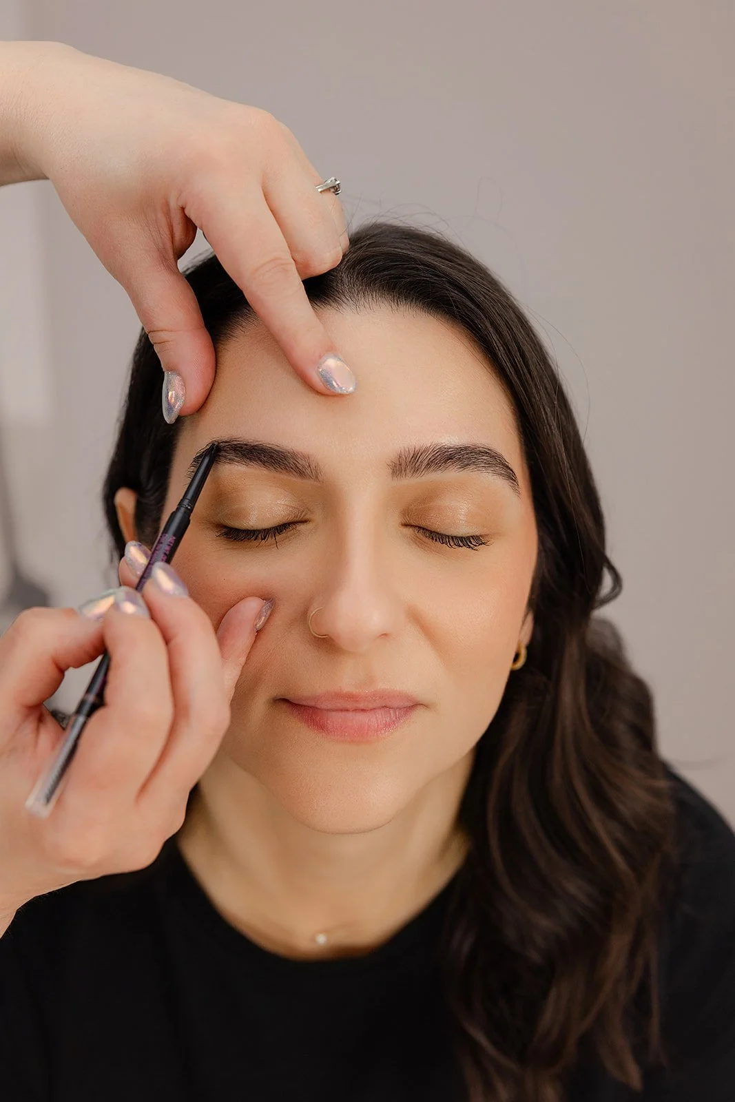 A woman with closed eyes getting her eyebrows filled in with makeup during a beauty treatment.
