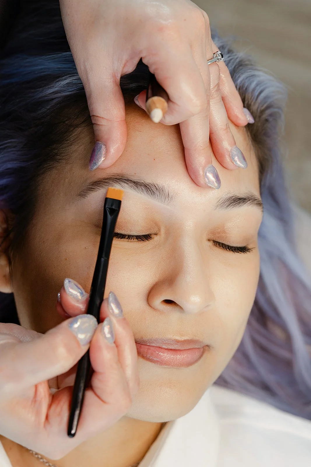 A person having their eyebrows shaped or painted by a cosmetologist during a beauty treatment.