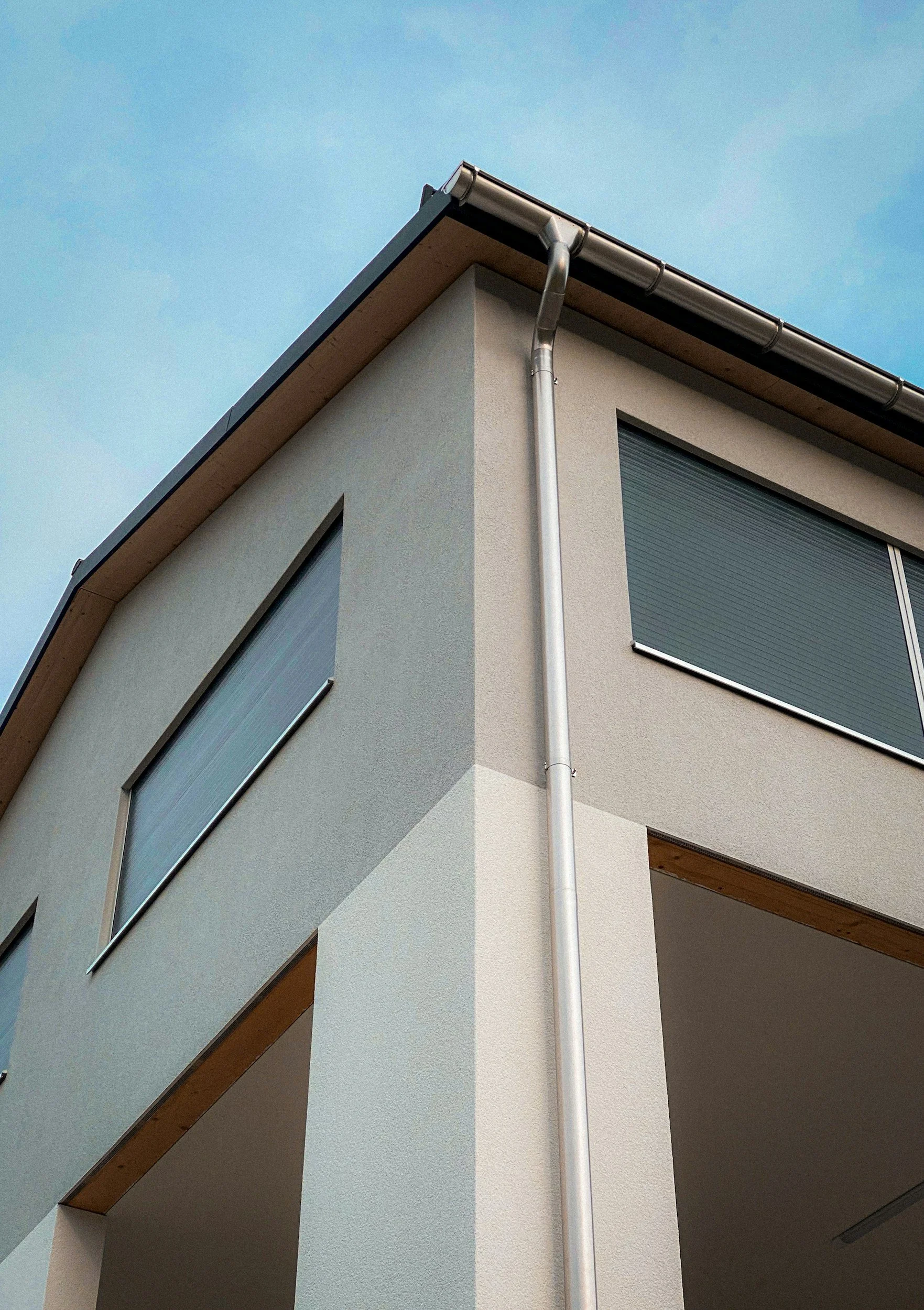 Close-up of a modern house corner with a gutter and downspout against a blue sky.