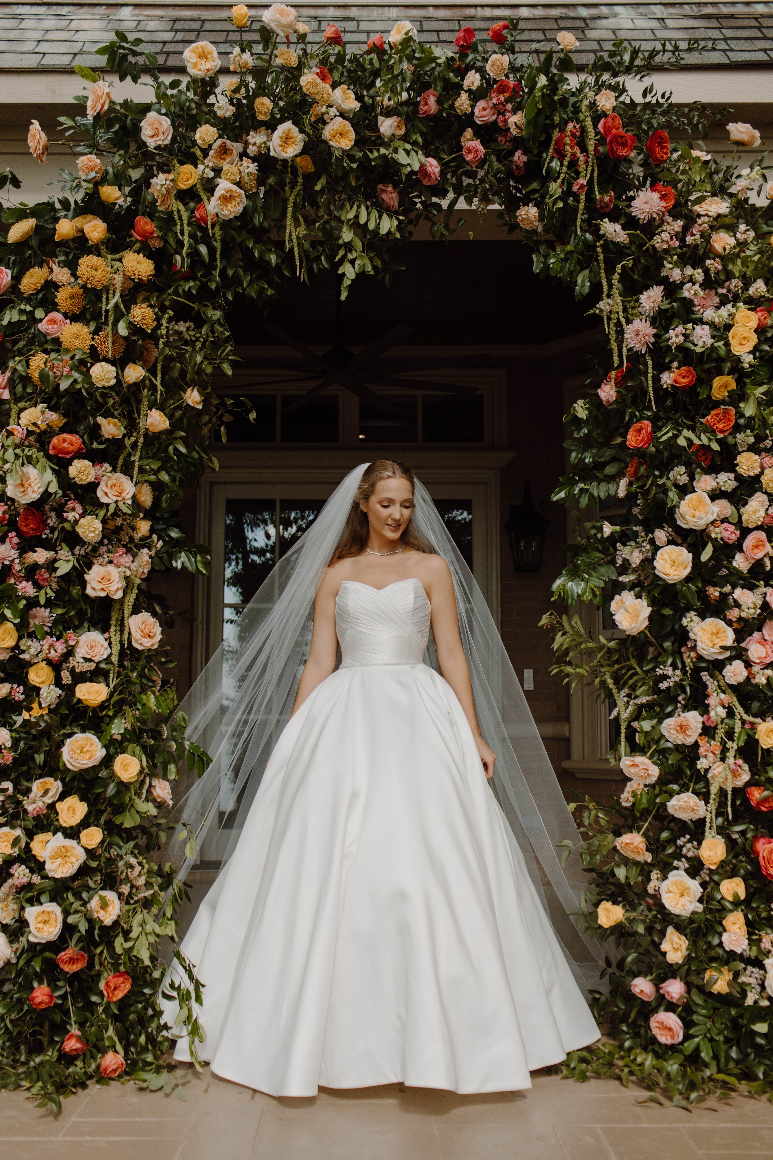 Bridal portrait - a bride in a wedding gown standing under a luxury floral archway.