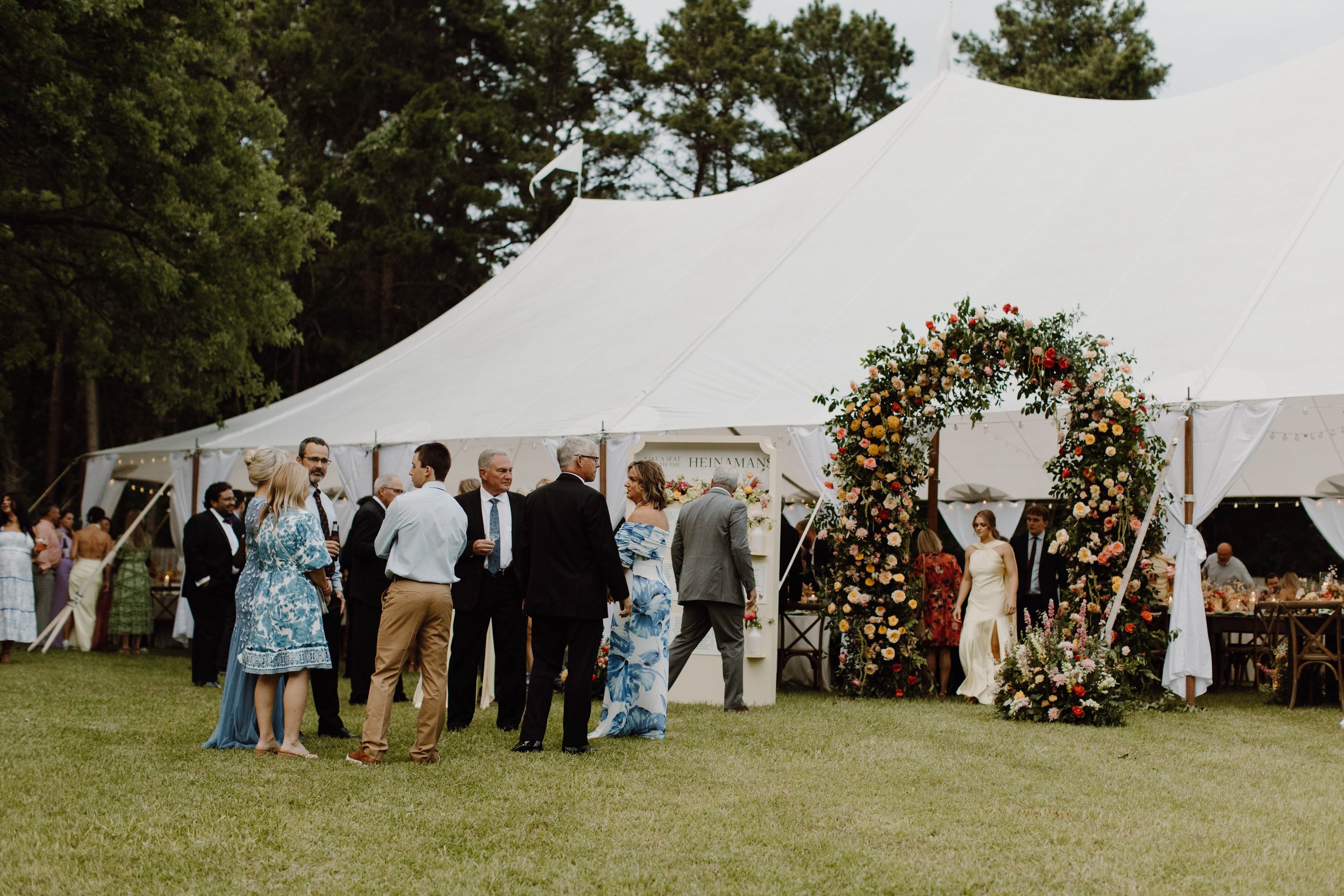 Elevated White tent wedding reception hall - beautiful floral arch - the wedding guests gathering and mingling. Telling the whole story from front to back.