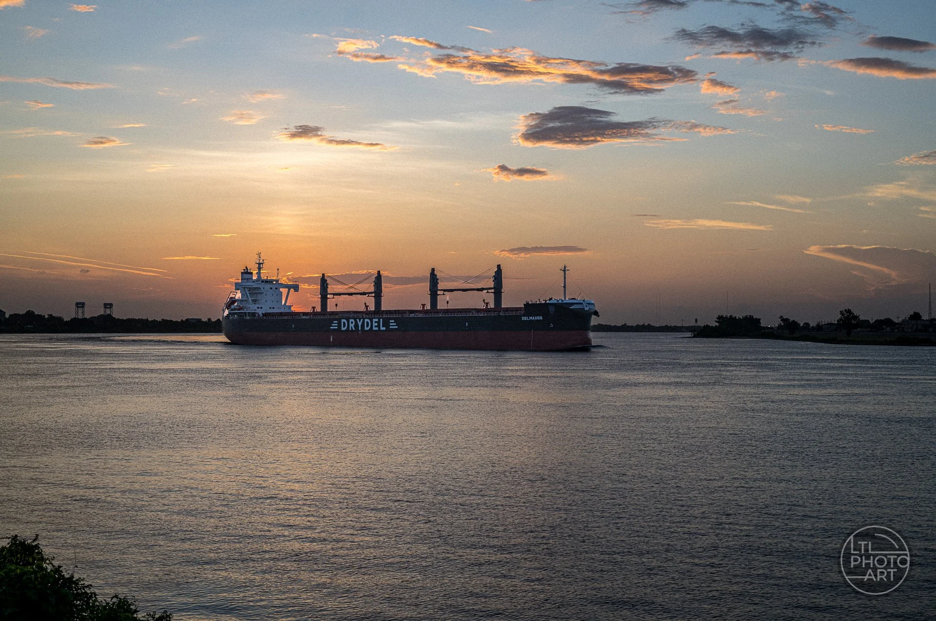 Cargo ship traveling along the Mississippi River at sunrise in New Orleans beneath a warm, cloud-filled sky.