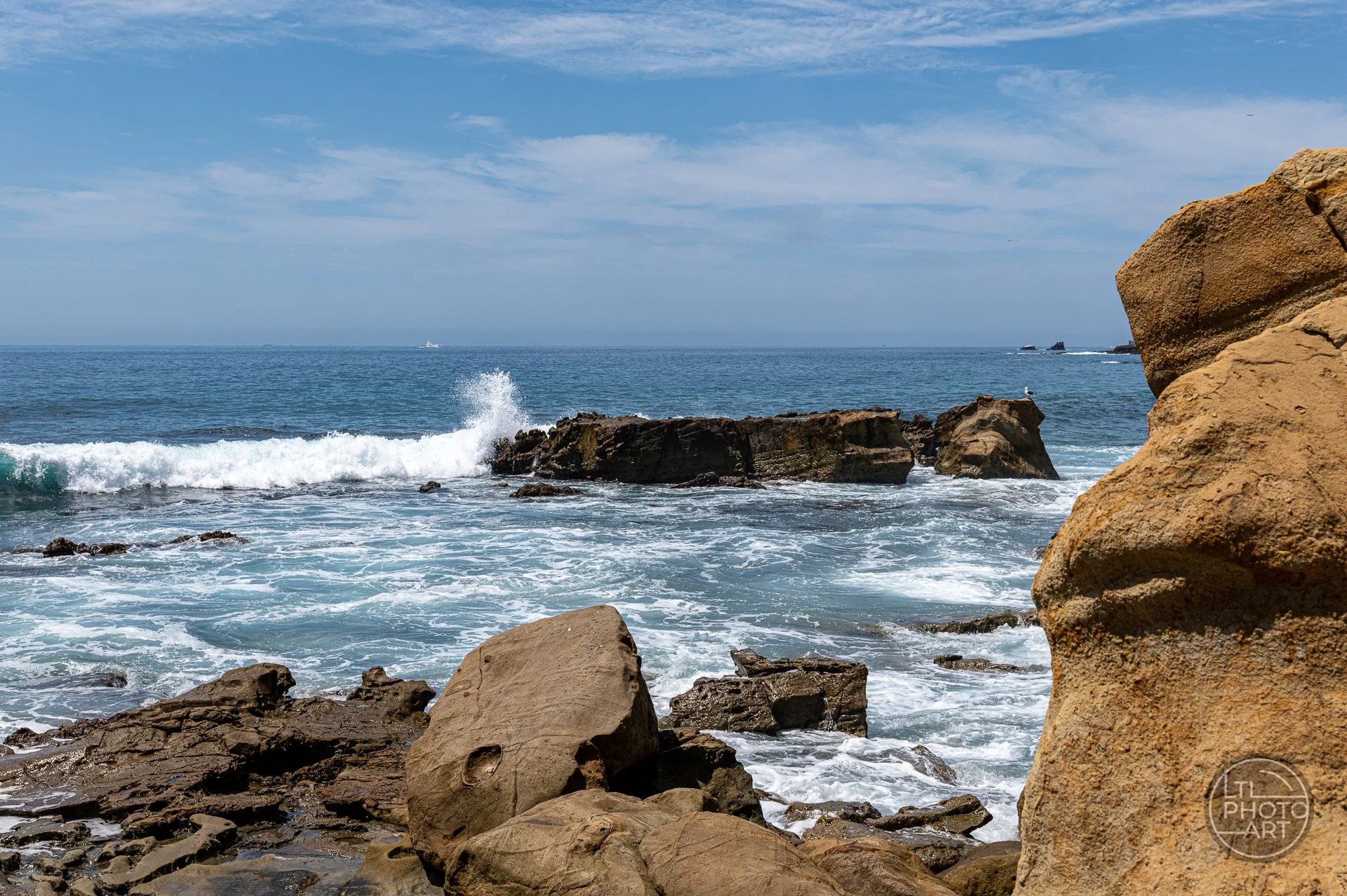 Sea-level view from the bottom of the Monument Point stairs with rocky shoreline and breaking waves in Laguna Beach, California.