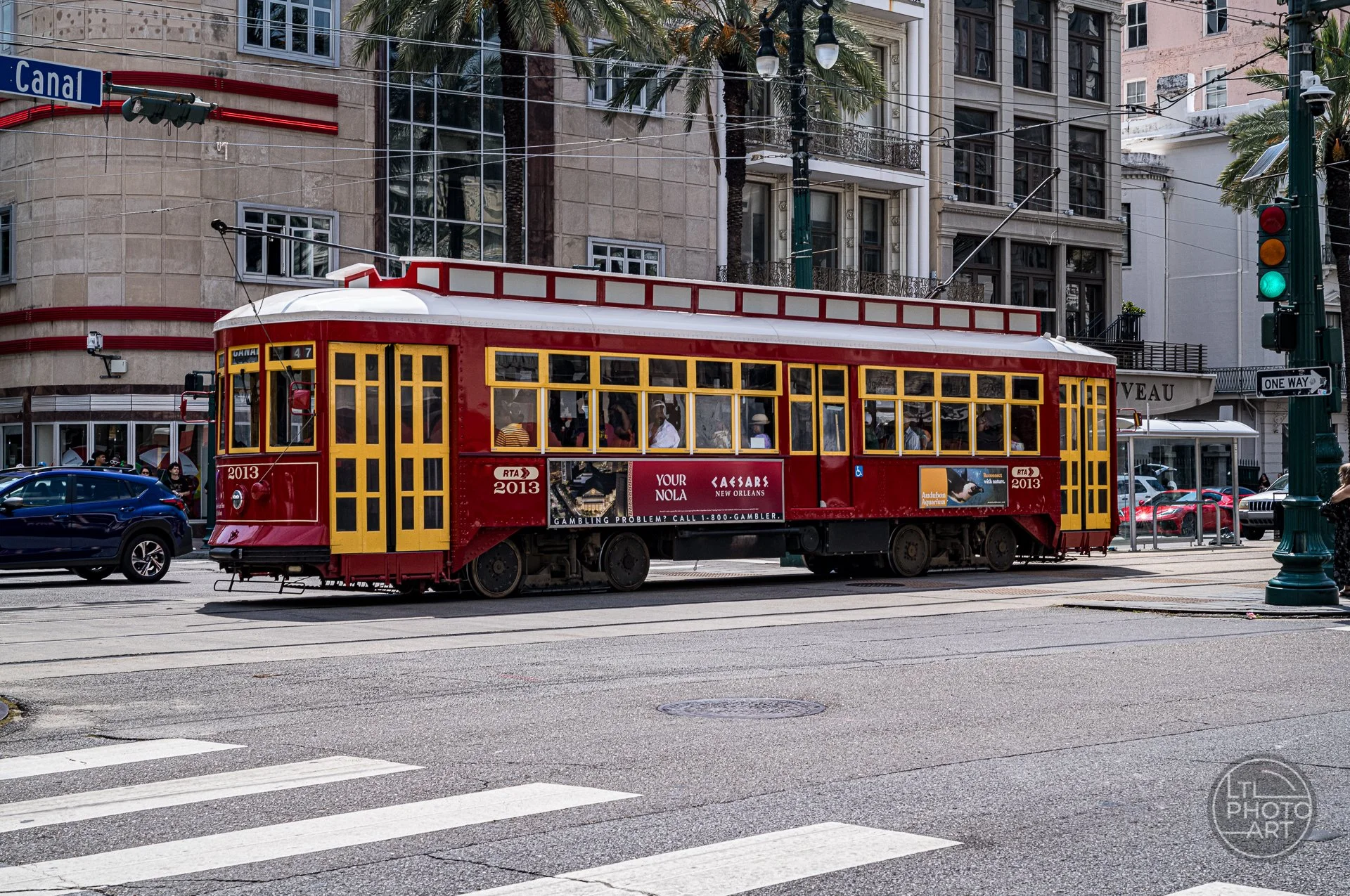 Red Canal Streetcar traveling through downtown New Orleans near Canal Street, with palm trees, buildings, traffic lights, and city traffic.