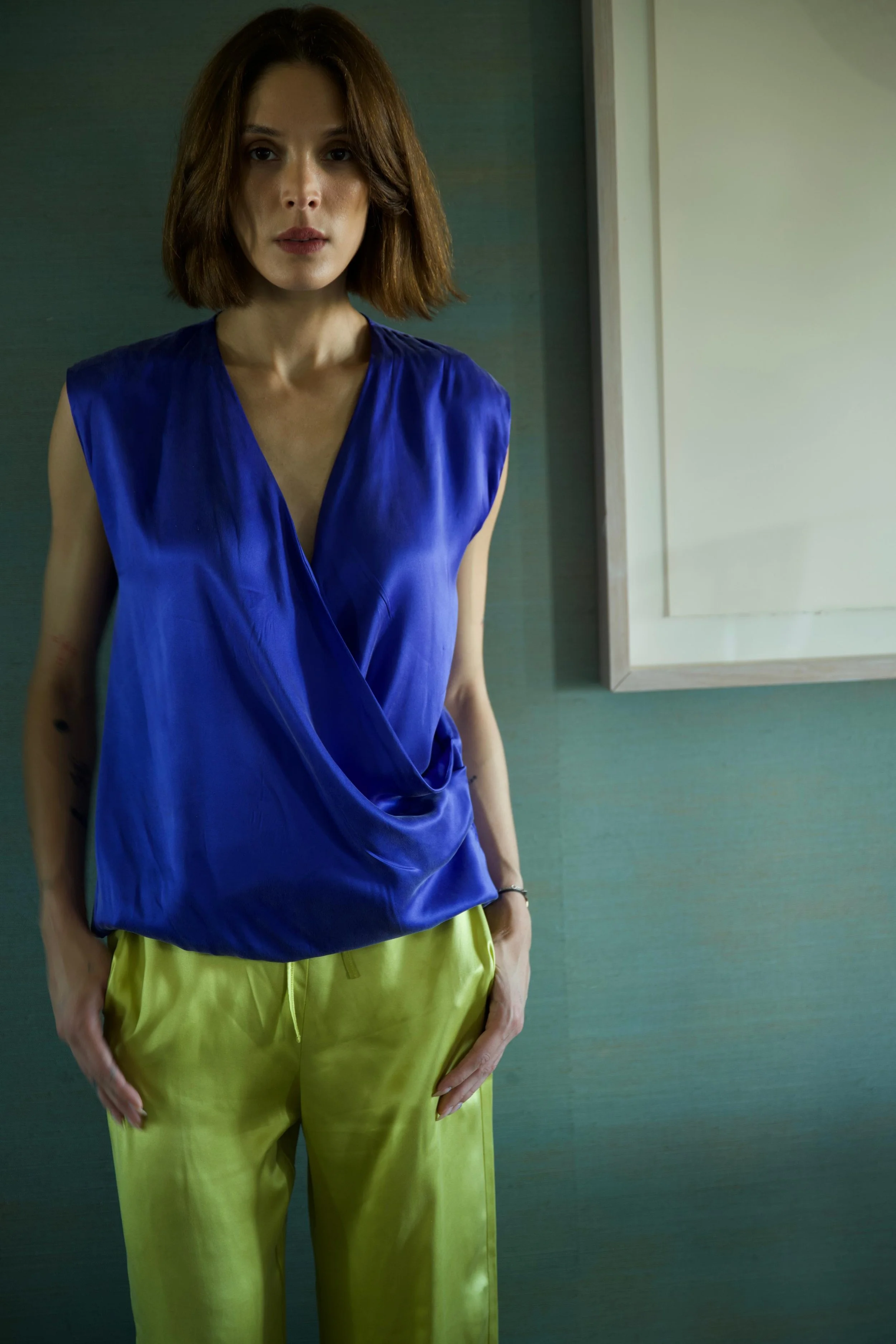 Woman wearing blue draped silk top and lemon trousers