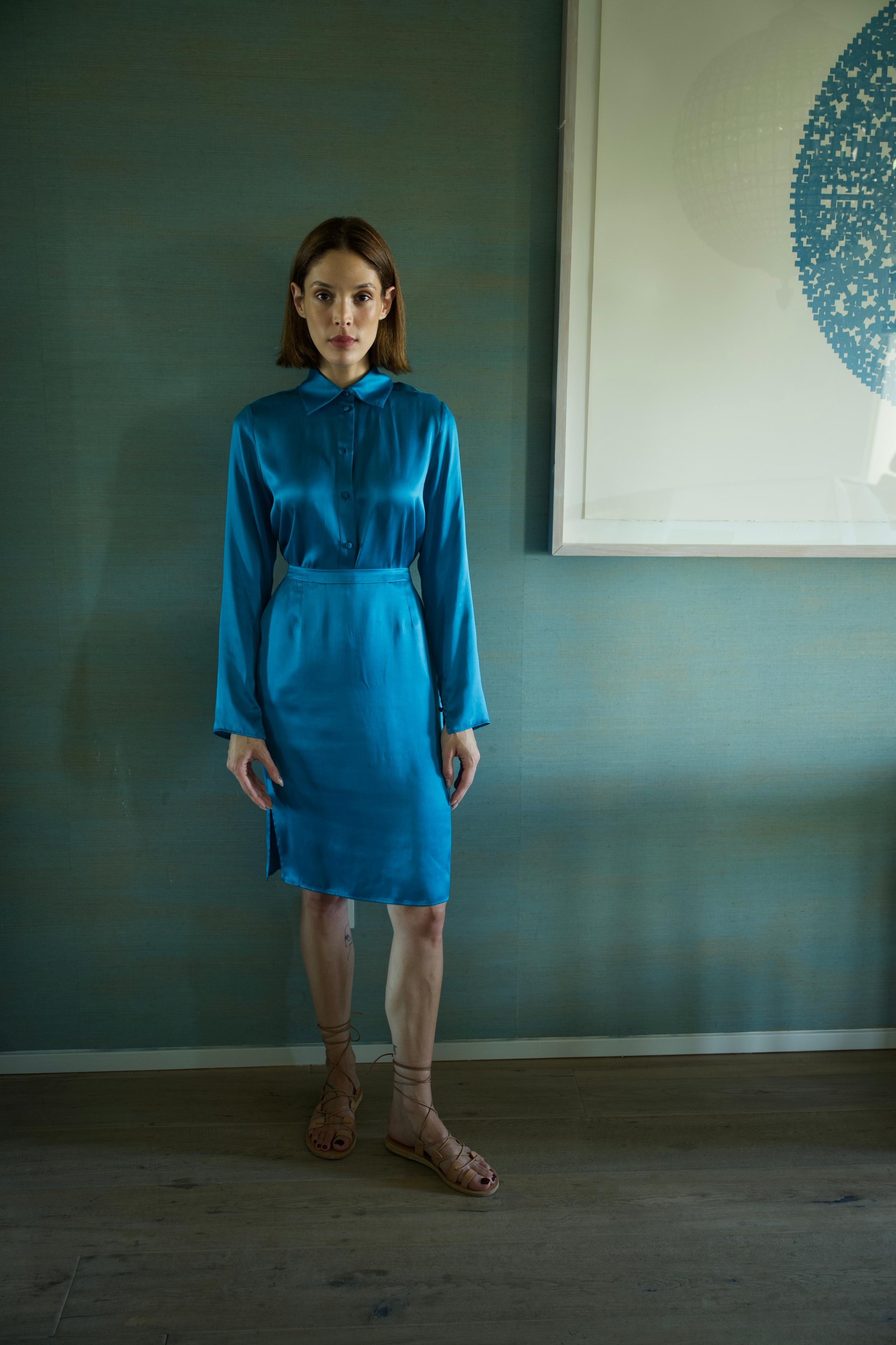 oman wearing blue silk shirt and skirt near framed artwork